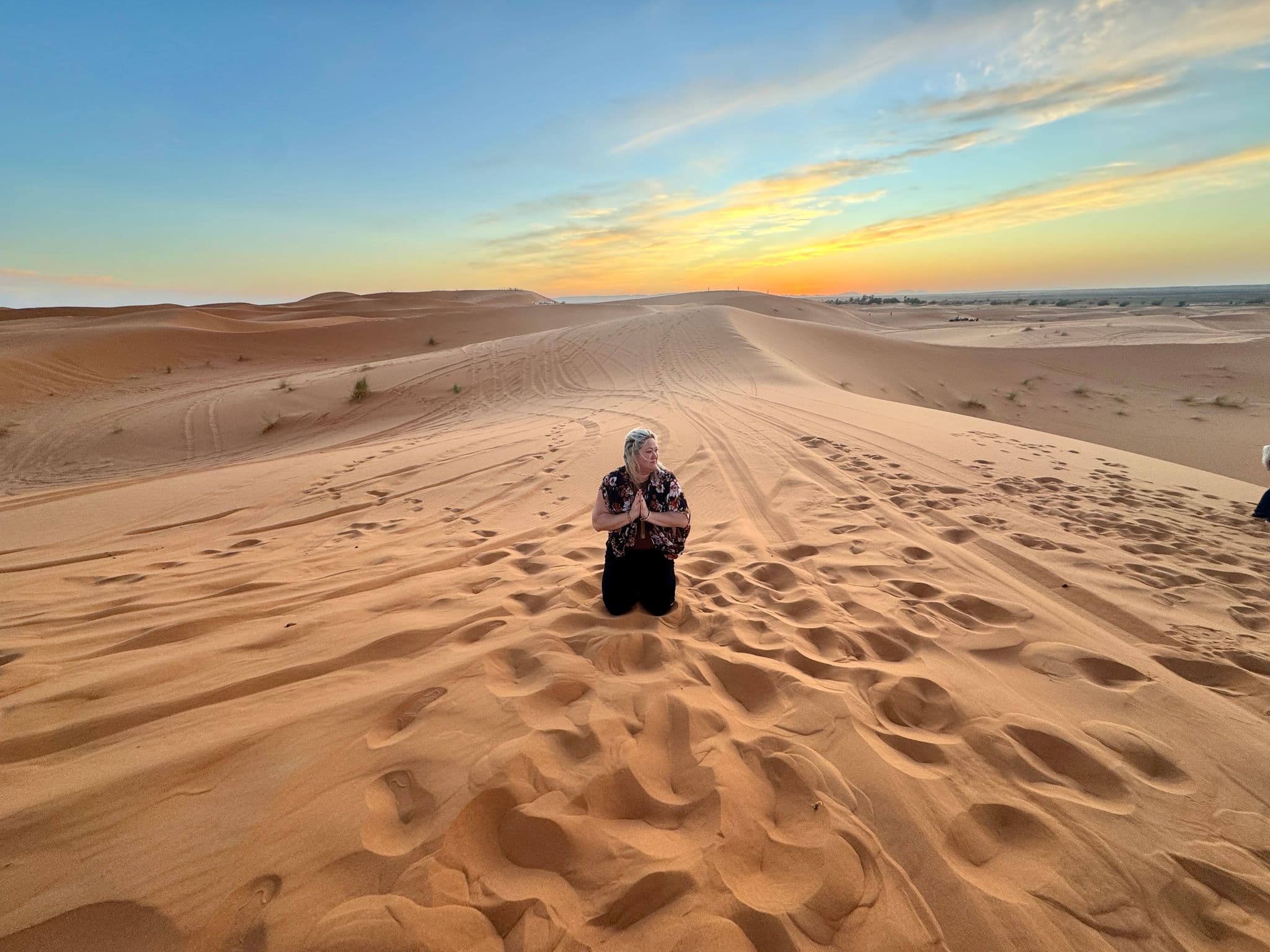 Sand dunes at sunset with a person kneeling in the foreground on a desert trip.