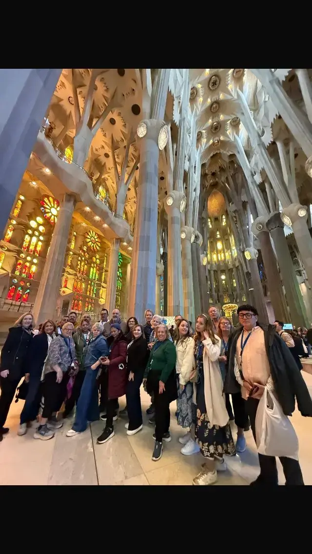 Interior of the Sagrada Família in Barcelona, Spain, with a tour group posing beneath colorful stained-glass windows and tall columns.