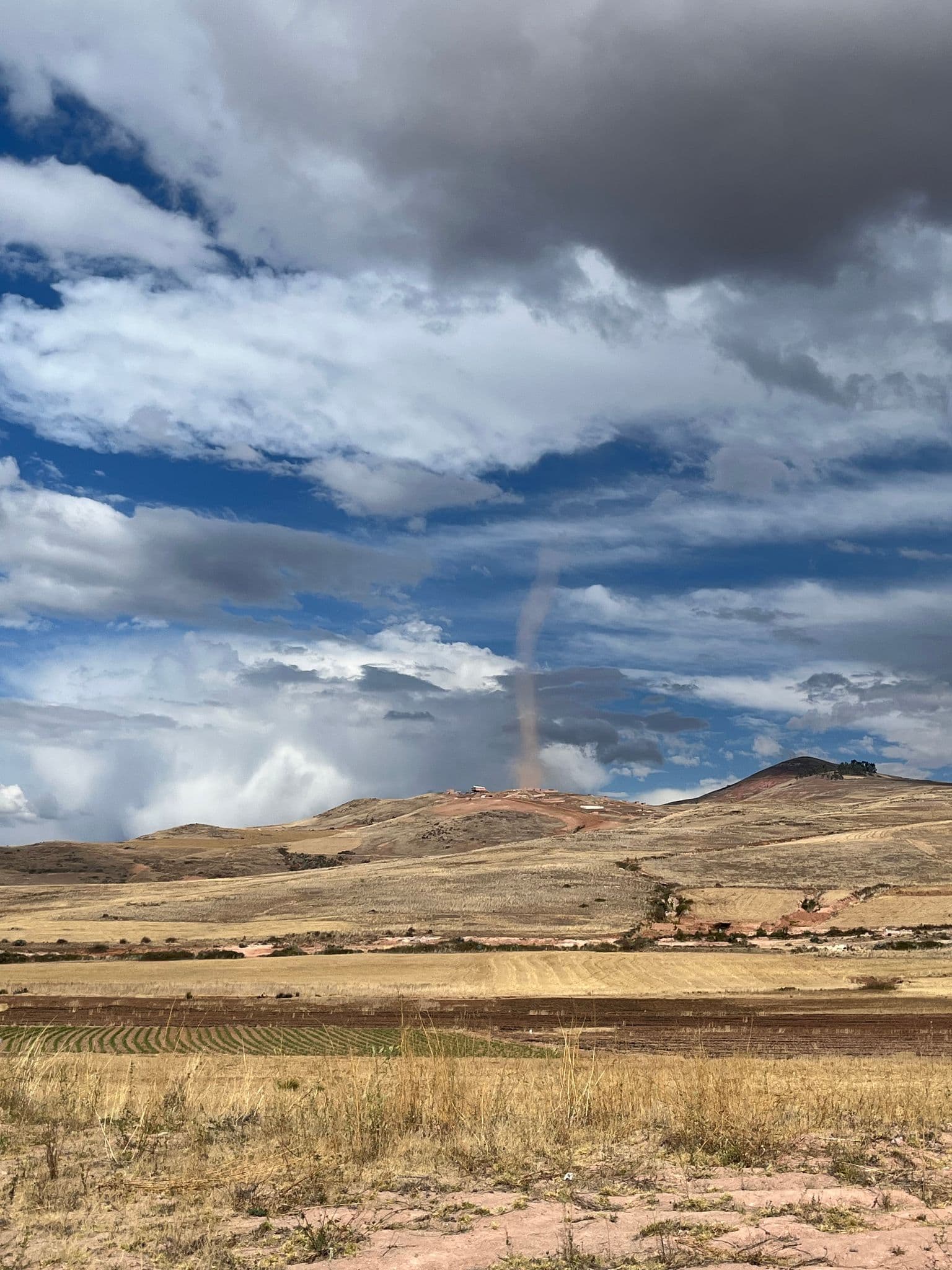 Dust devil funnel over rolling hills and cultivated fields in the Peruvian highlands, Peru.