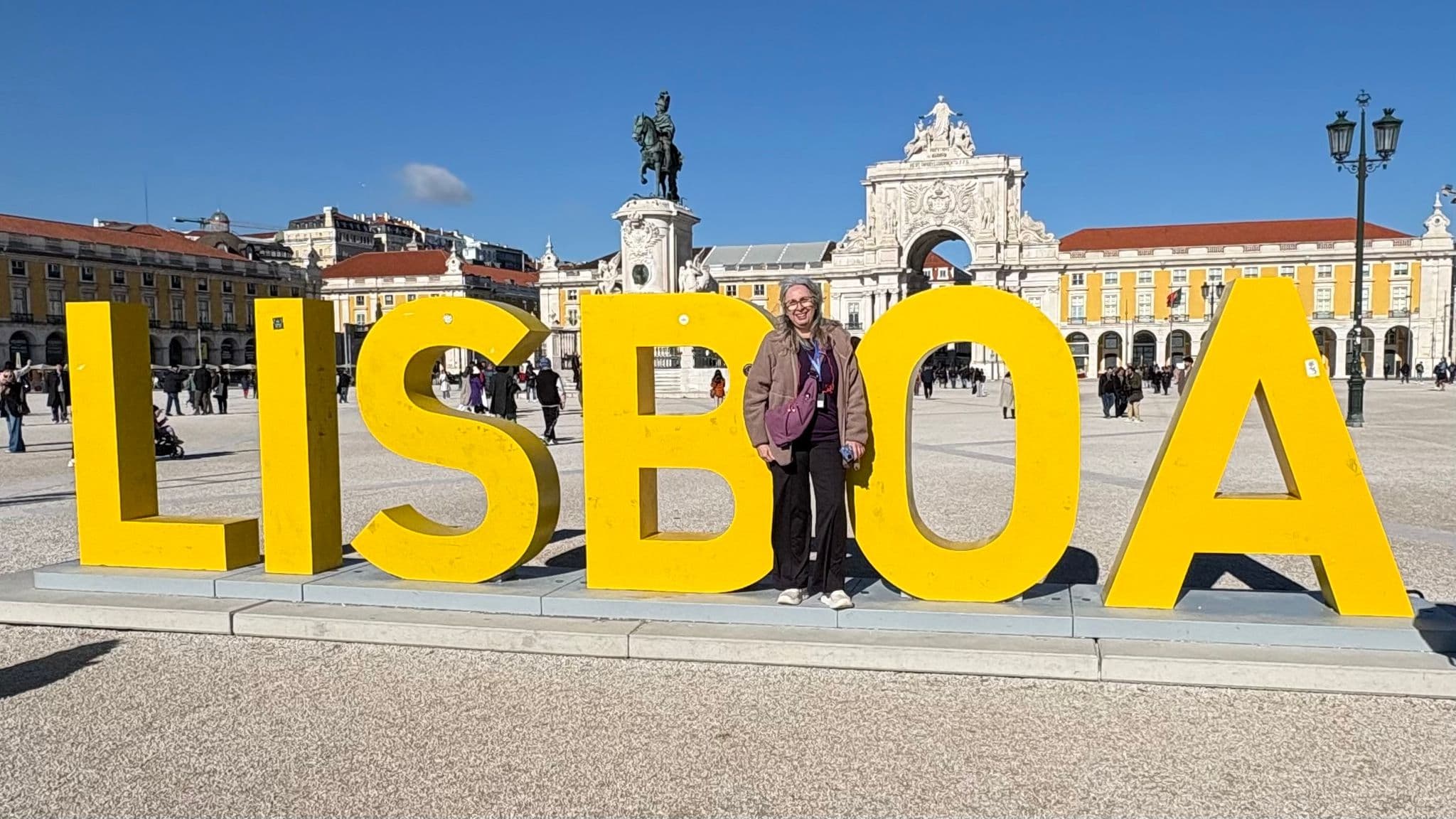 Large yellow LISBOA letters with a person standing in the O at Praça do Comércio, Lisbon, Portugal.