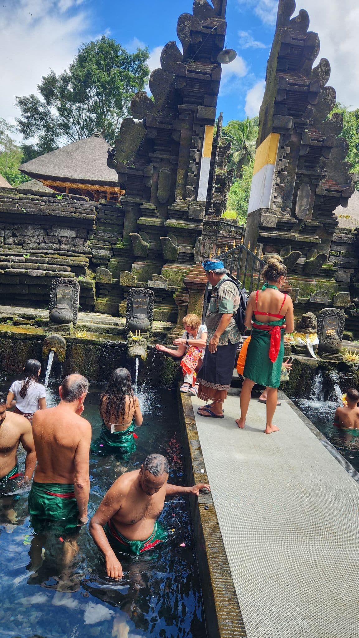 Tirta Empul Temple purification fountains in Bali, Indonesia with travelers bathing under stone spouts during a ritual.