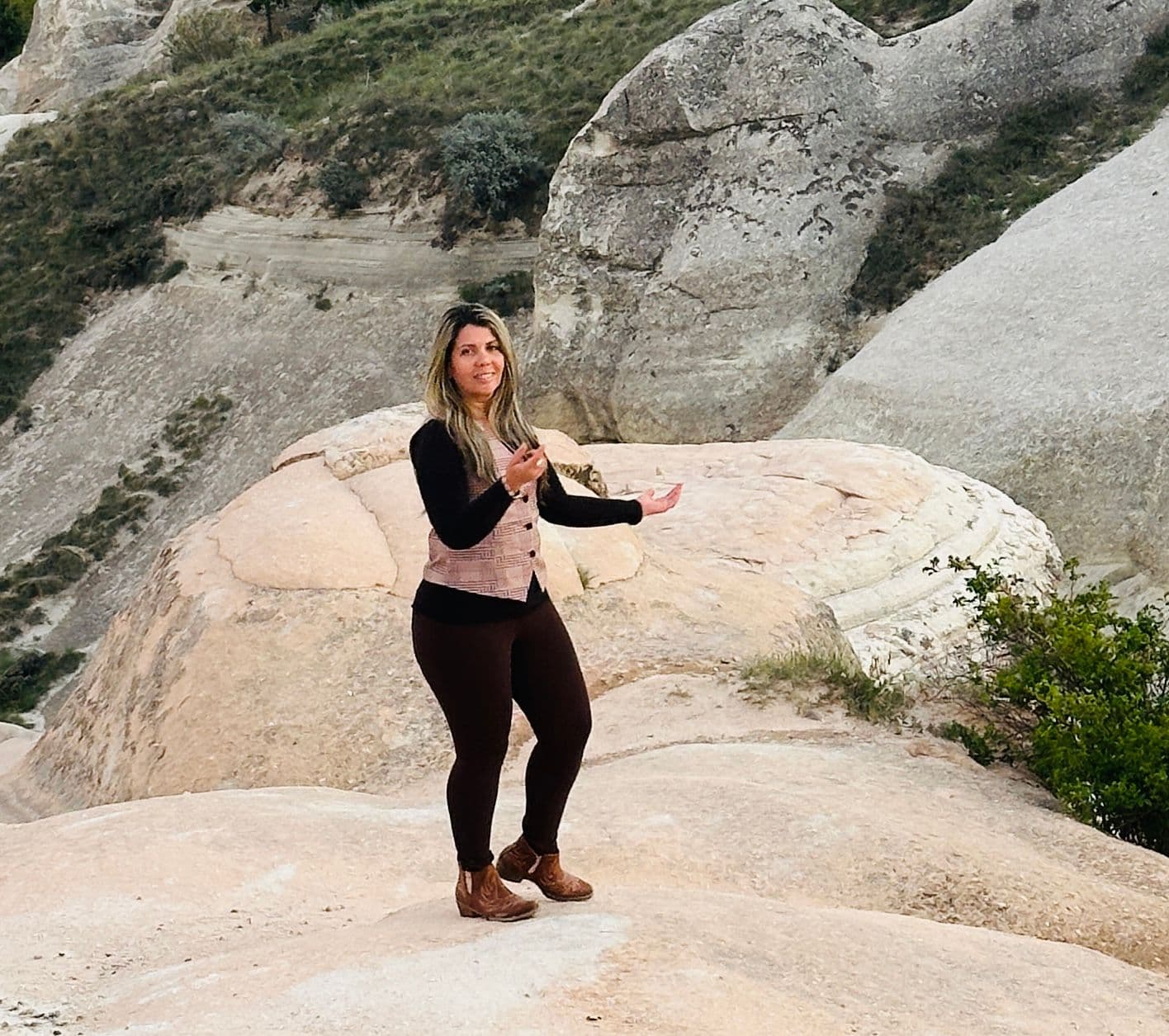 Cappadocia rock formations with a woman standing and gesturing on a pale rock during a trip in Cappadocia, Turkey.