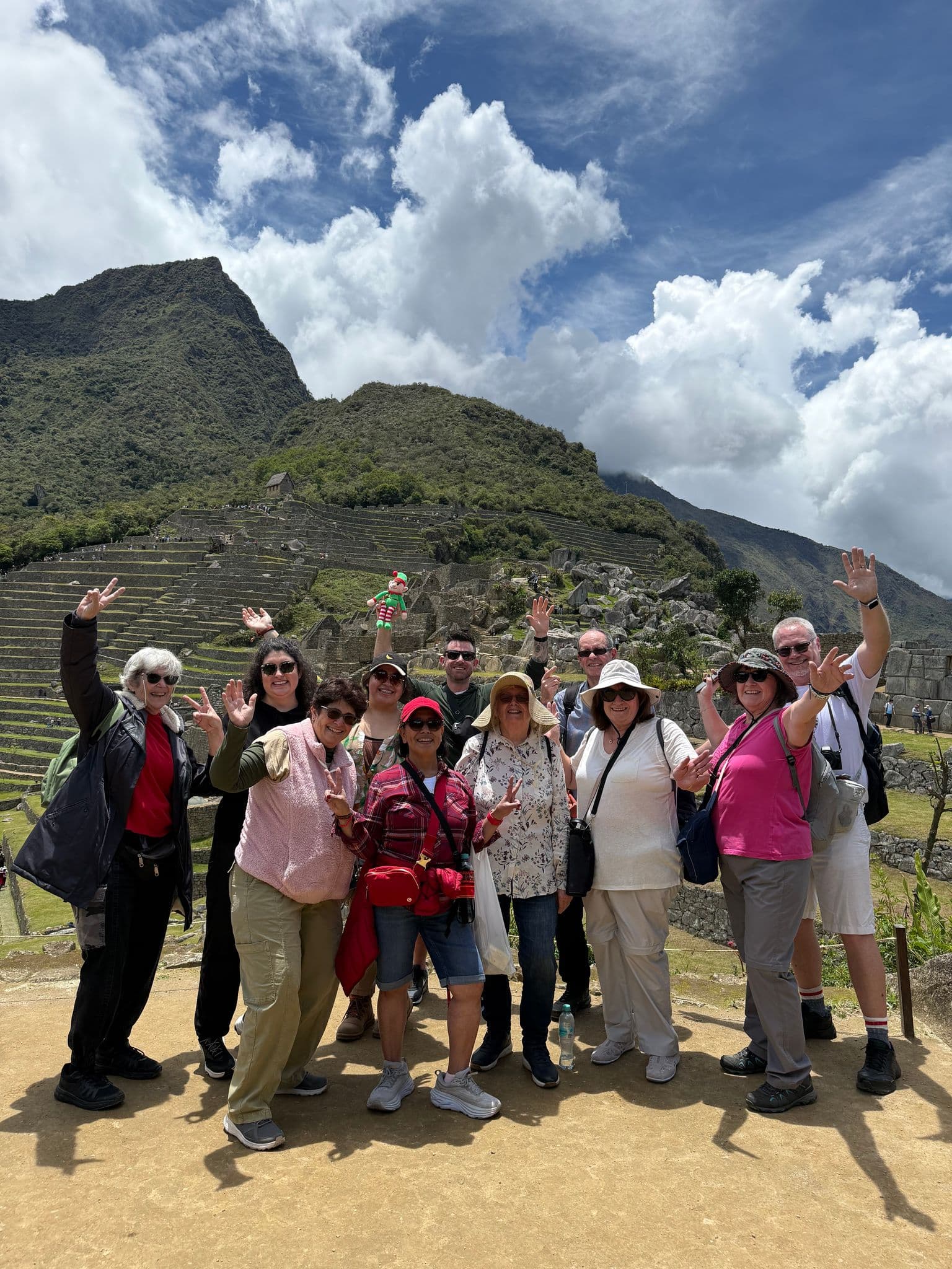 Machu Picchu ruins with a group of travelers posing and waving on a tour in the Cusco region, Peru.