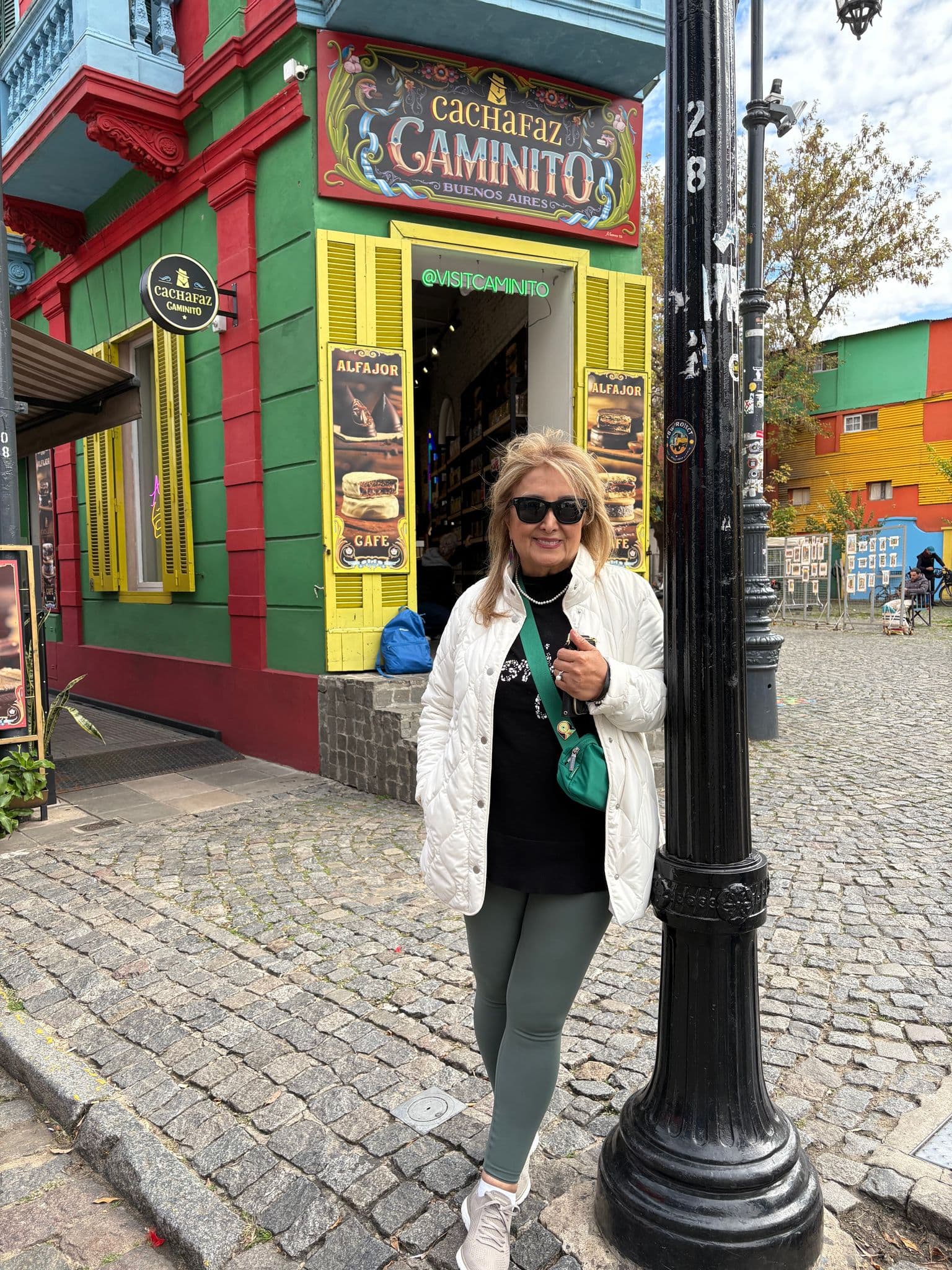 Caminito storefront and colorful houses with a woman standing by a lamp post on the cobbled street in La Boca, Buenos Aires, Argentina.