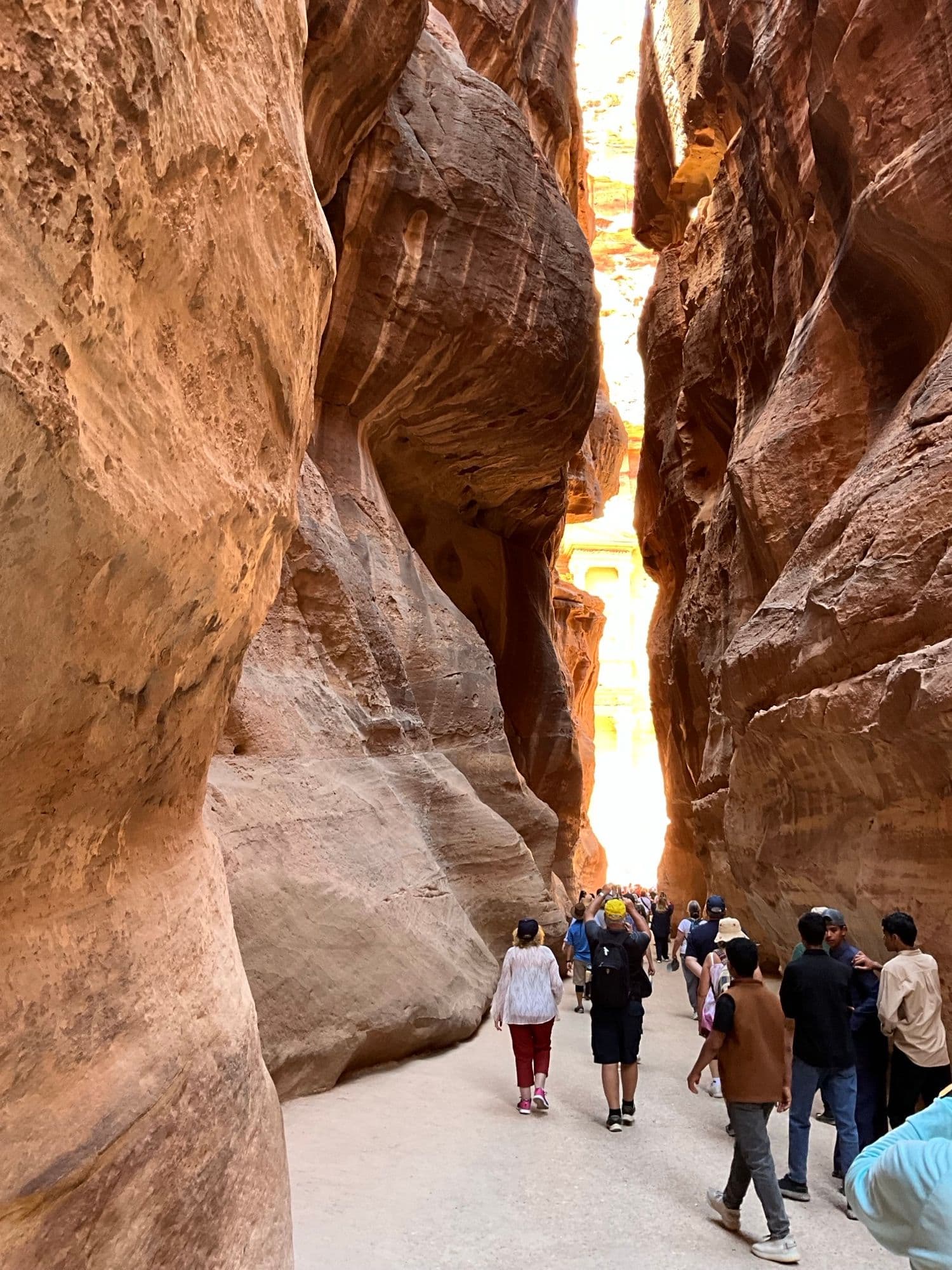 The Treasury (Al-Khazneh) framed by the narrow Siq in Petra, Jordan, with tourists walking toward it.