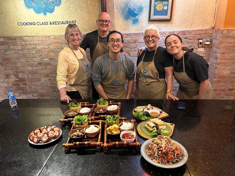 A group of five people standing behind a table of prepared Vietnamese dishes at a cooking class in Ho Chi Minh City, Vietnam.