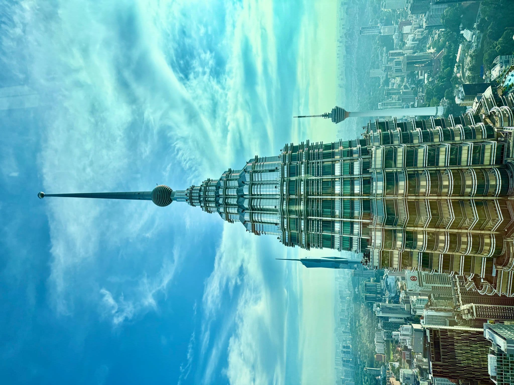 Petronas Twin Towers spire and upper levels rising above the Kuala Lumpur skyline with Menara Kuala Lumpur visible to the side, Malaysia.