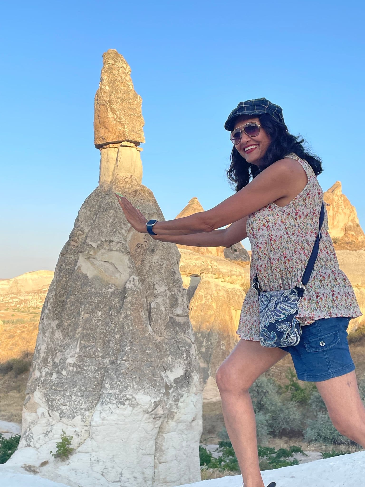 Fairy chimney in Cappadocia with a woman posing as if pushing it during a trip in Turkey.
