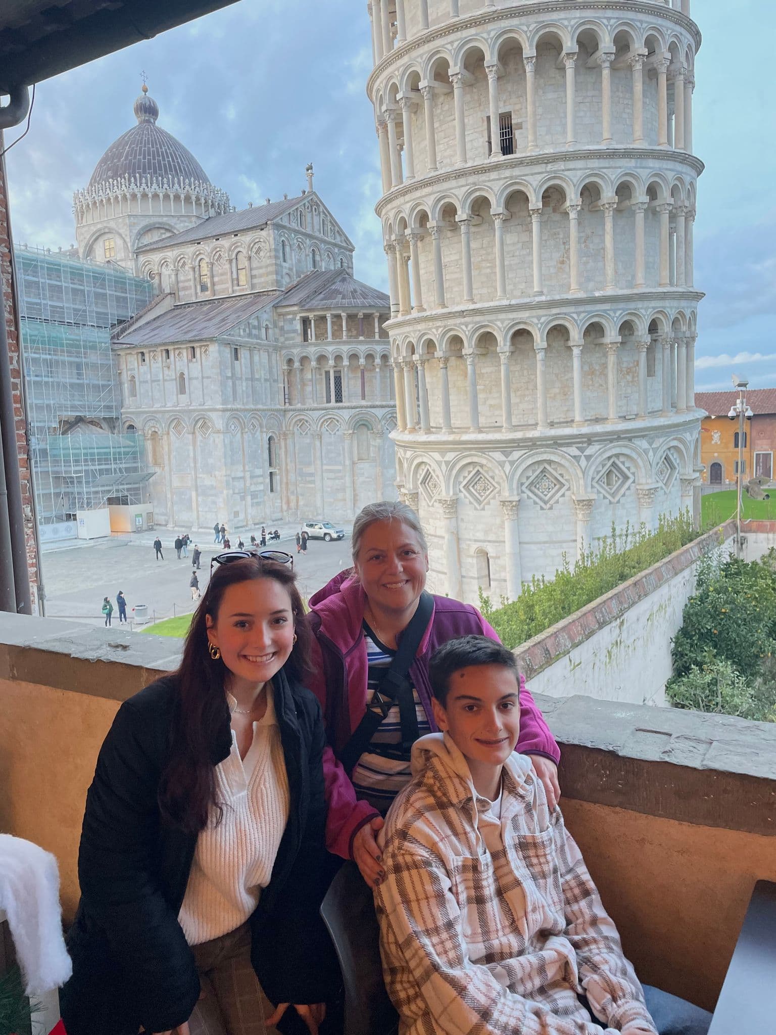 Leaning Tower of Pisa behind three family members posing together on a balcony in Pisa, Italy.