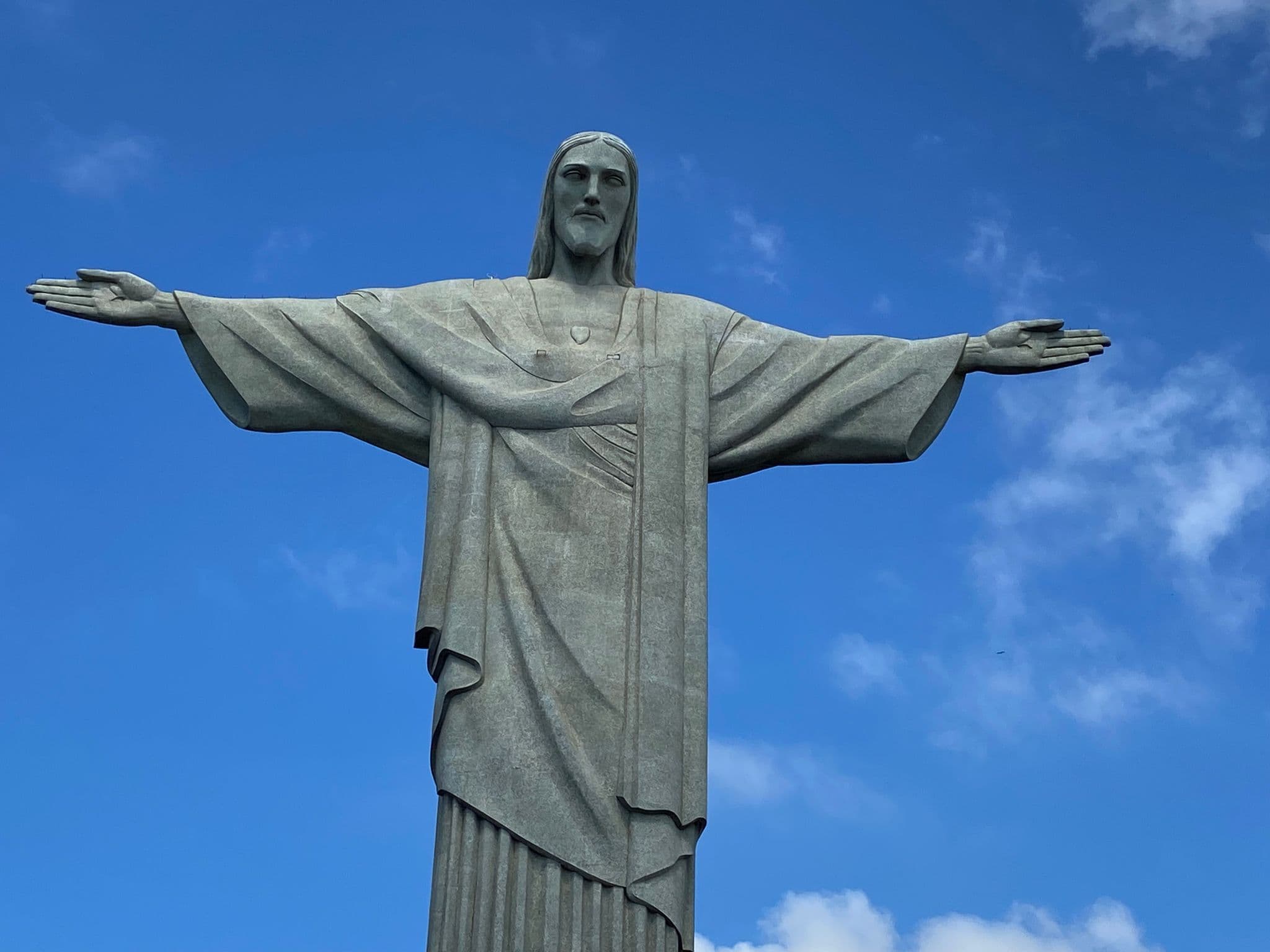 Christ the Redeemer statue with outstretched arms above Rio de Janeiro, Brazil against a clear blue sky.