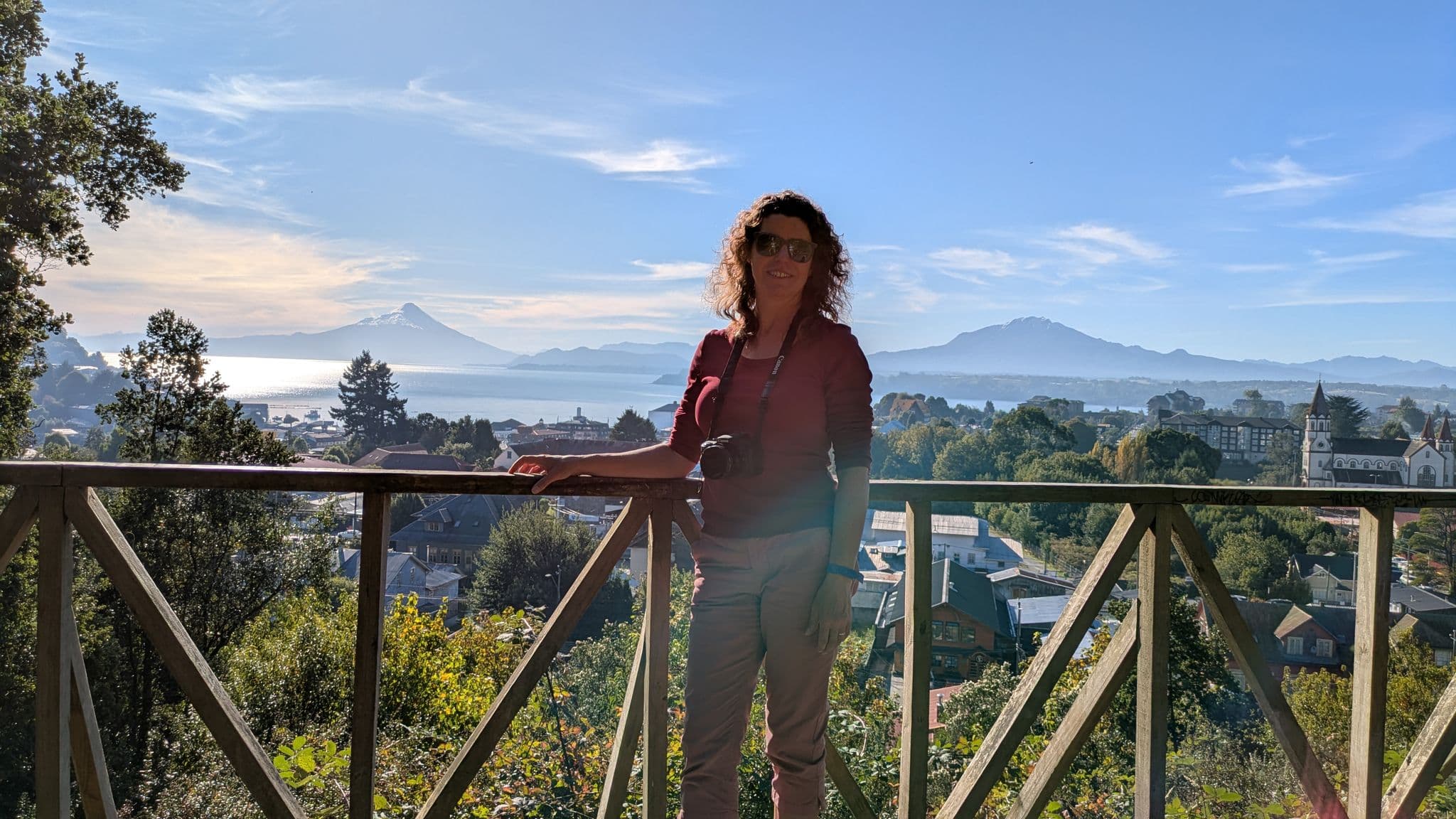 Osorno Volcano and Lake Llanquihue with a traveler leaning on a wooden railing overlooking Puerto Varas, Chile.