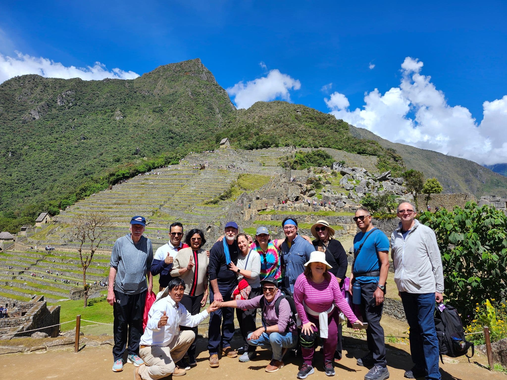 Machu Picchu terraces with a group of travelers posing together on a sunny day, Cusco region, Peru.