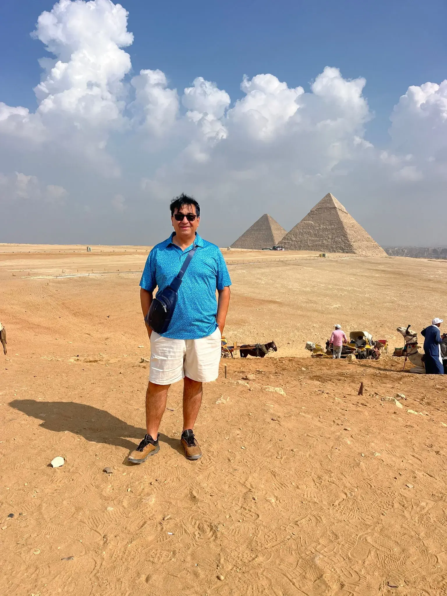 Pyramids of Giza behind a tourist standing on the desert with camels and handlers visible on the horizon, Giza, Egypt