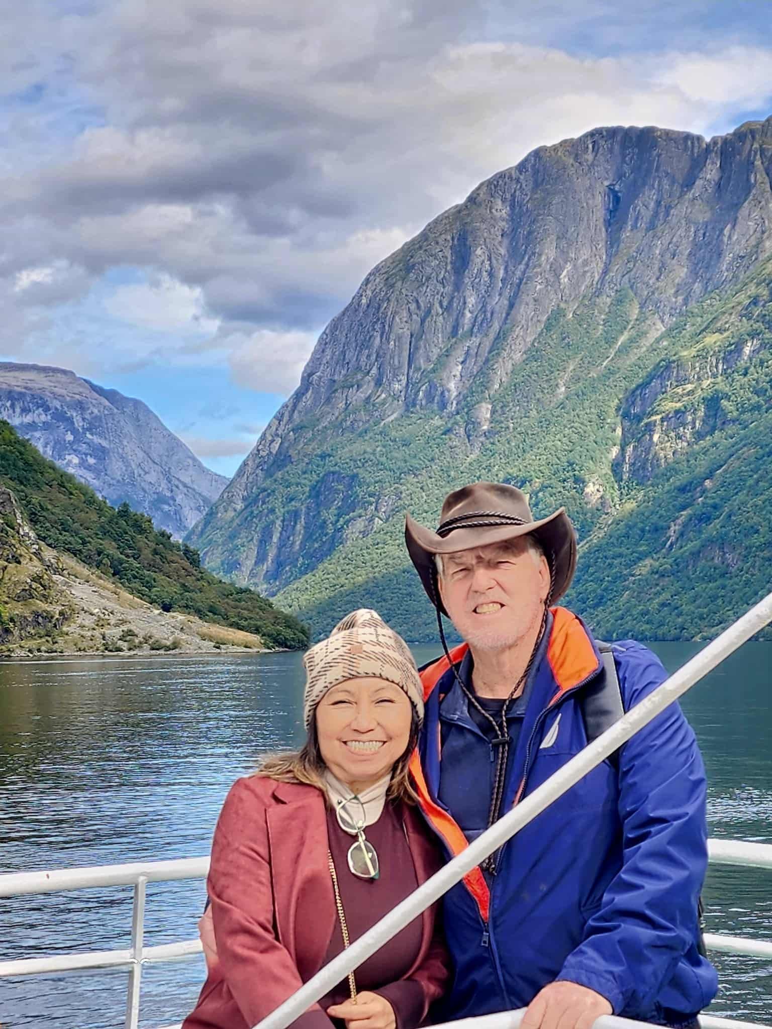 Steep fjord cliffs with a smiling couple posing on a boat in Norway.