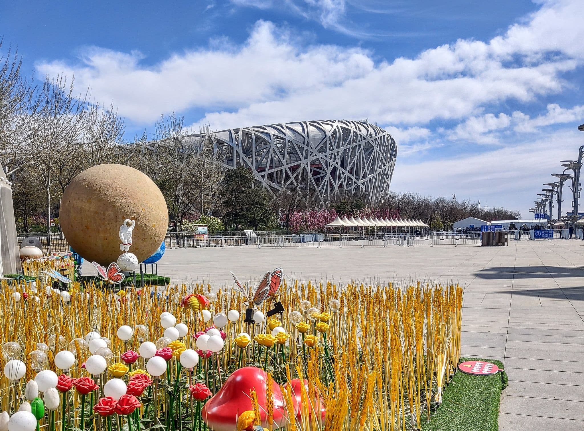 Beijing National Stadium (Bird's Nest) framed behind decorative flowers and planet sculptures on a plaza in Beijing, China.