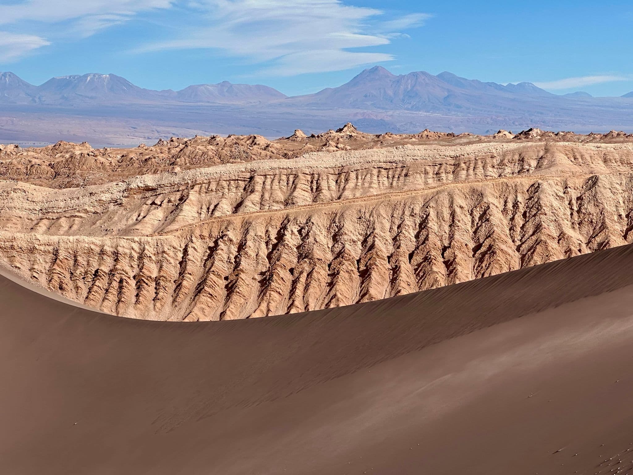 Valle de la Luna dunes and eroded salt and stone formations with distant volcanoes in the Atacama Desert, Chile.