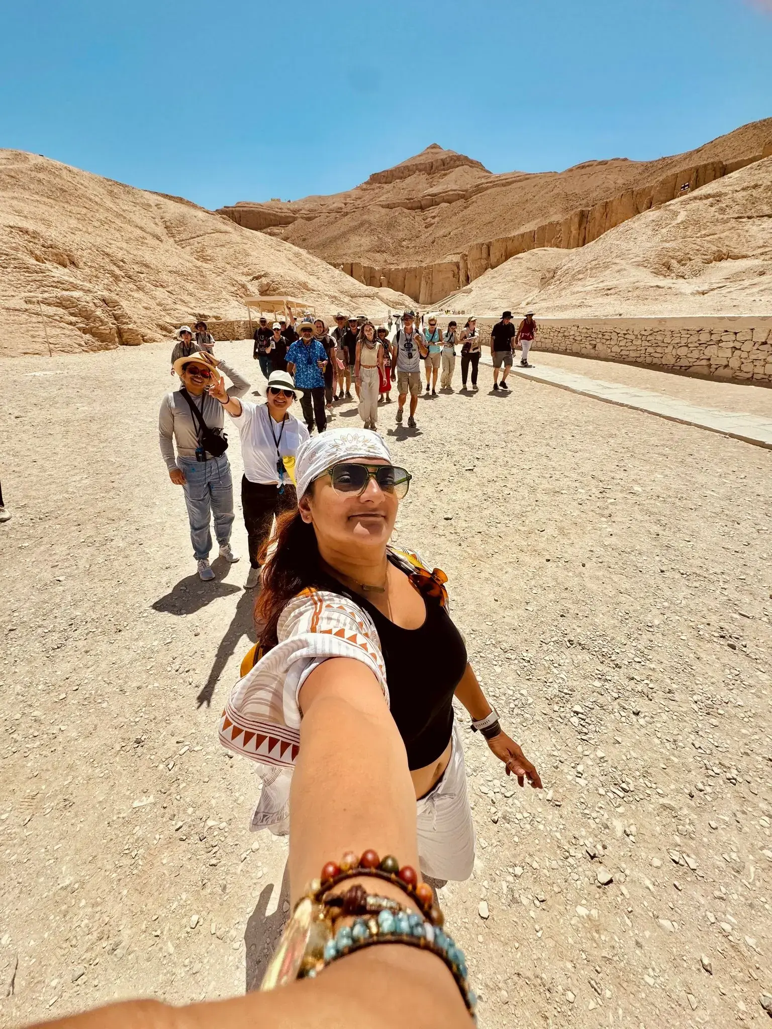 Valley of the Kings, Luxor, Egypt with a woman taking a selfie as a tour group walks behind her through the desert valley.