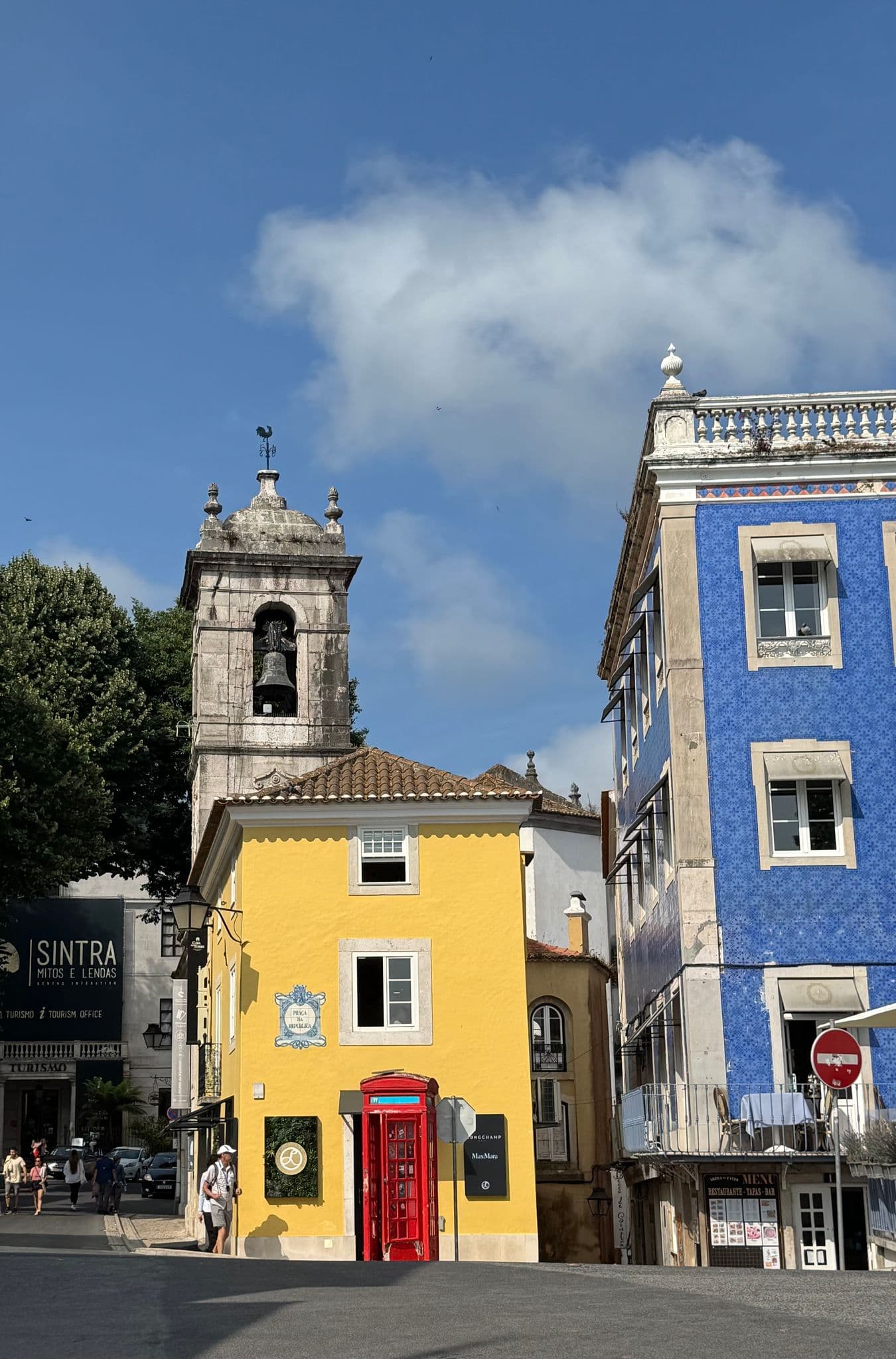Colorful buildings in Sintra historic center with a bell tower, a red phone booth, and people, Portugal.
