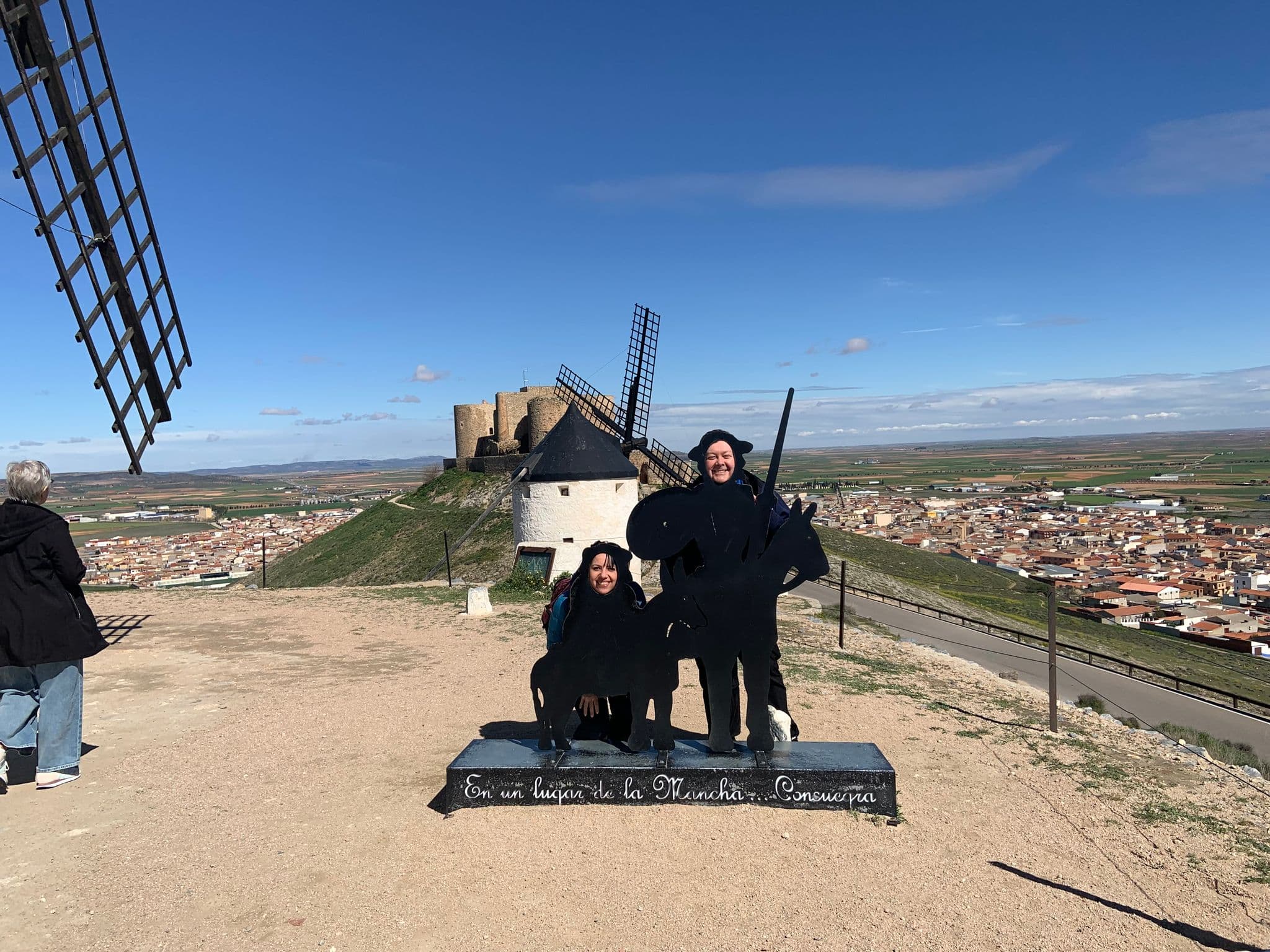 Consuegra windmills with two people posing behind a Don Quixote cutout on a hill above Consuegra, Spain.