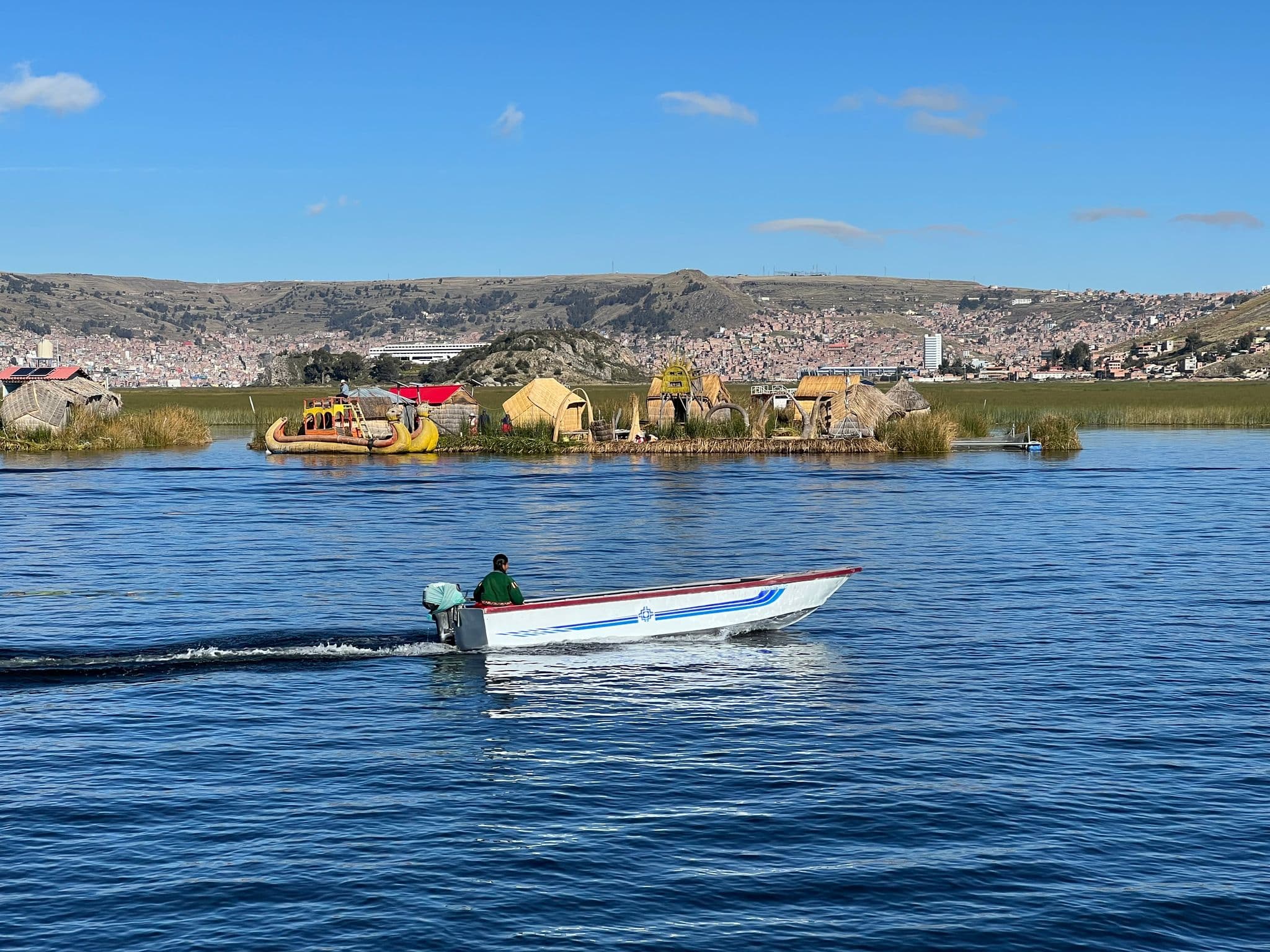 Uros floating reed islands with reed huts and a small motorboat crossing Lake Titicaca near Puno, Peru.