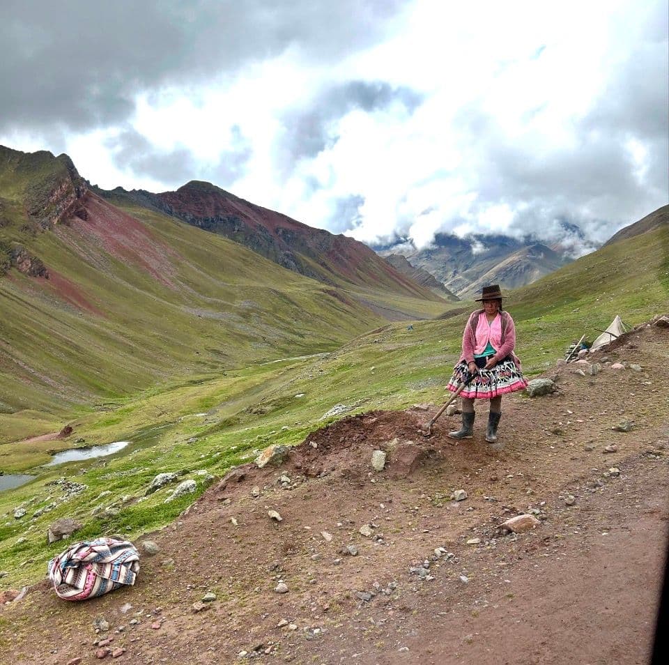 Rainbow Mountain (Vinicunca) valley with a woman in traditional clothing standing on a dirt path, Cusco region, Peru.