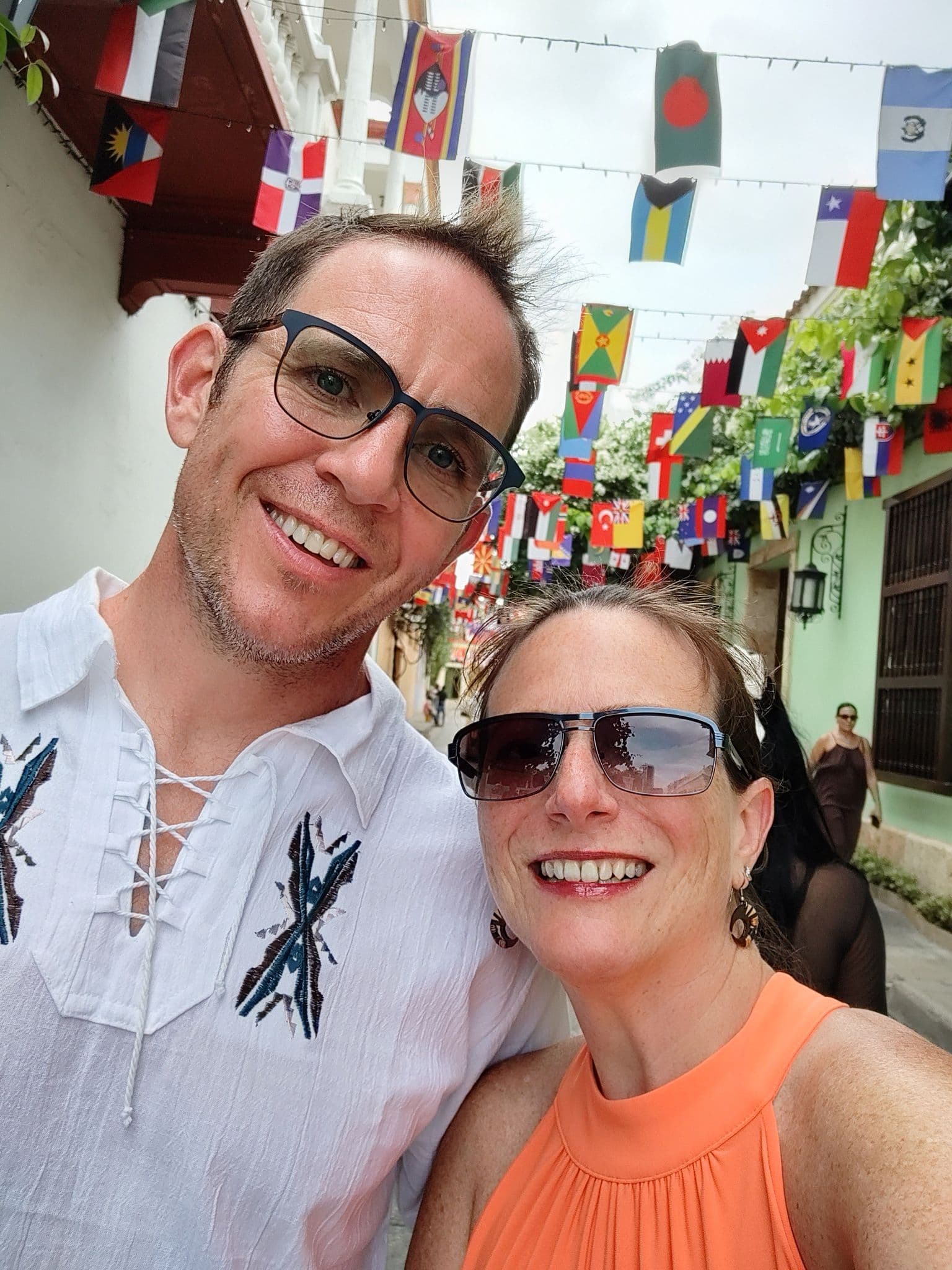 Smiling couple taking a selfie under hanging international flags in Cartagena Old Town, Colombia.