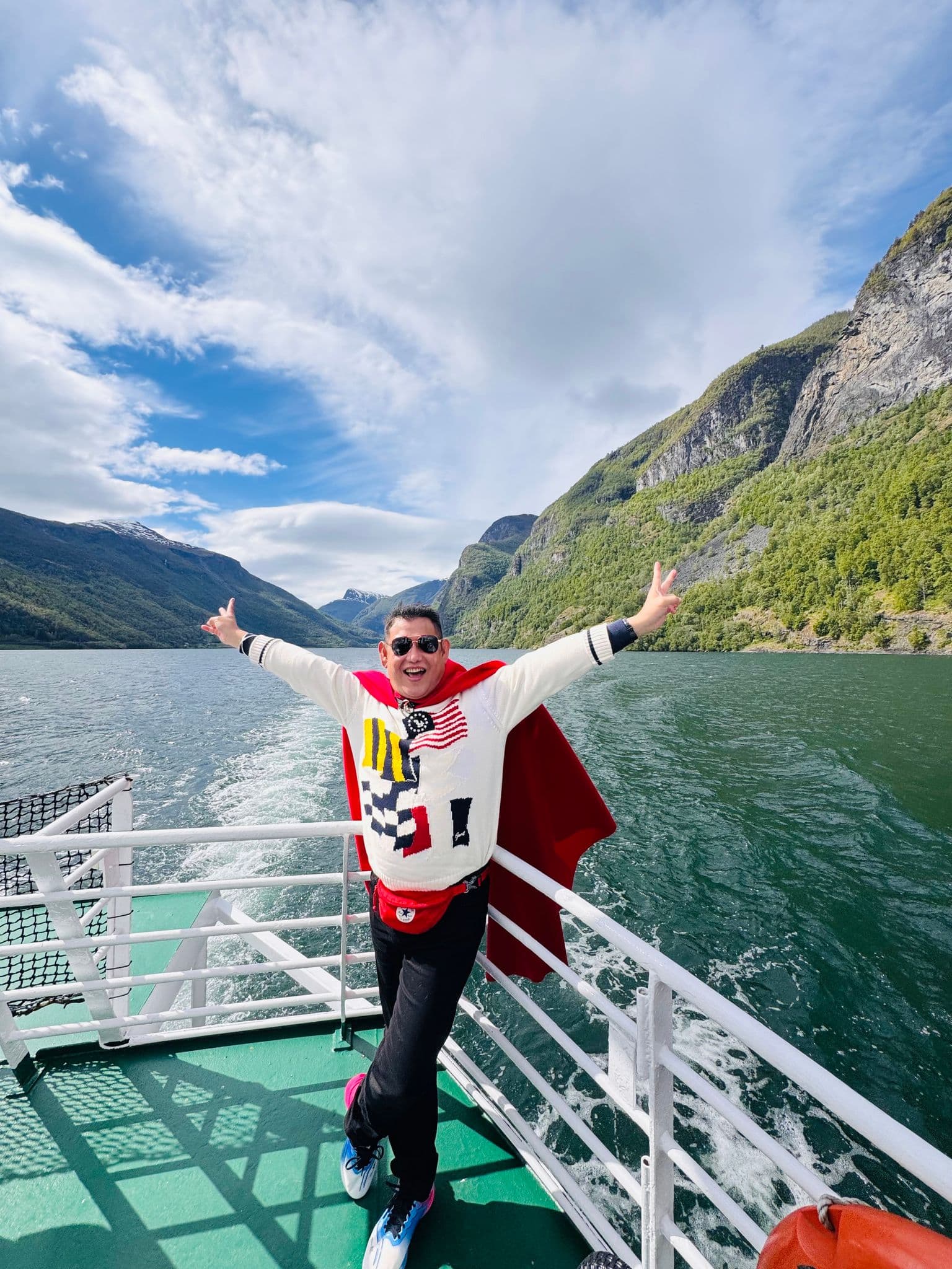 Norwegian fjords viewed from a ferry with a passenger spreading their arms, steep green mountains, Norway.