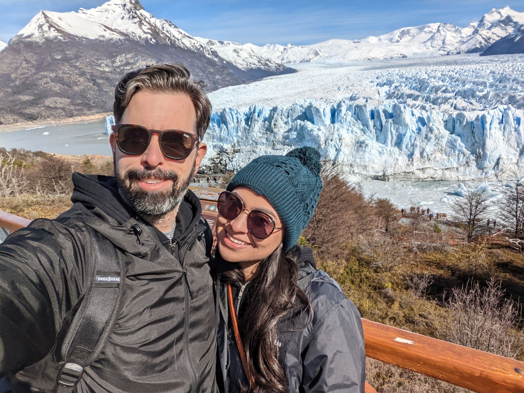Perito Moreno Glacier with a couple taking a selfie on a wooden viewing platform in El Calafate, Argentina.