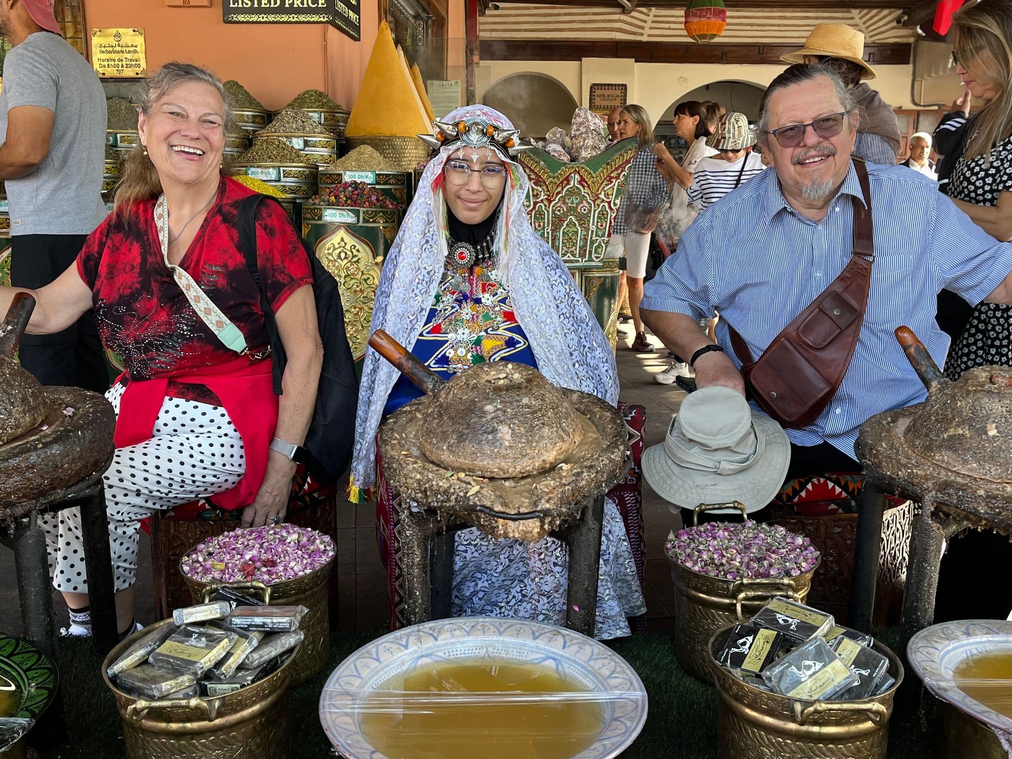 Spice stall at Jemaa el-Fnaa in Marrakech, Morocco with a woman in traditional dress seated between two tourists.