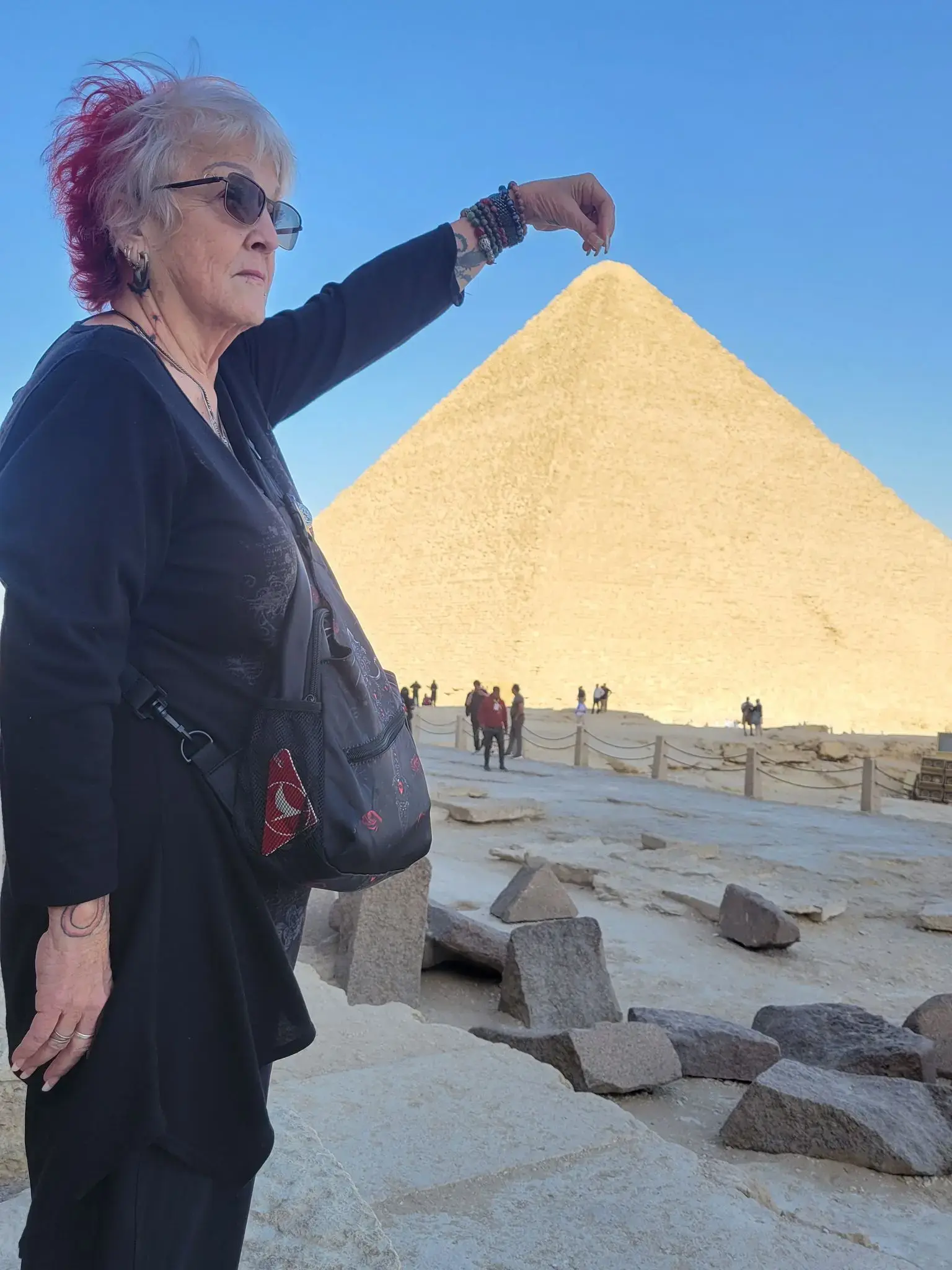Great Pyramid of Giza in Giza, Egypt with a woman appearing to pinch the pyramid's top while standing nearby.