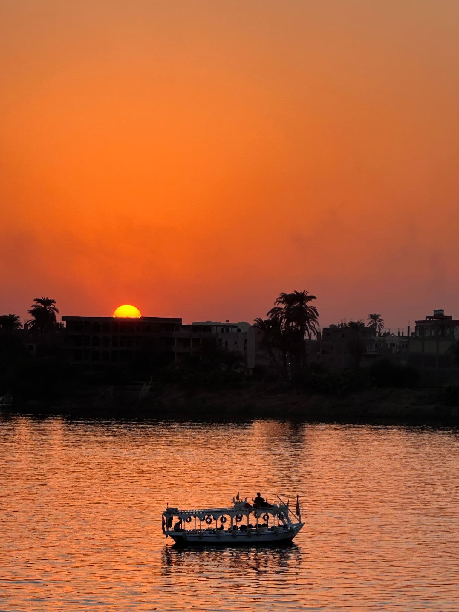 Sunset over the Nile River in Egypt with a small passenger boat crossing orange-reflected water.