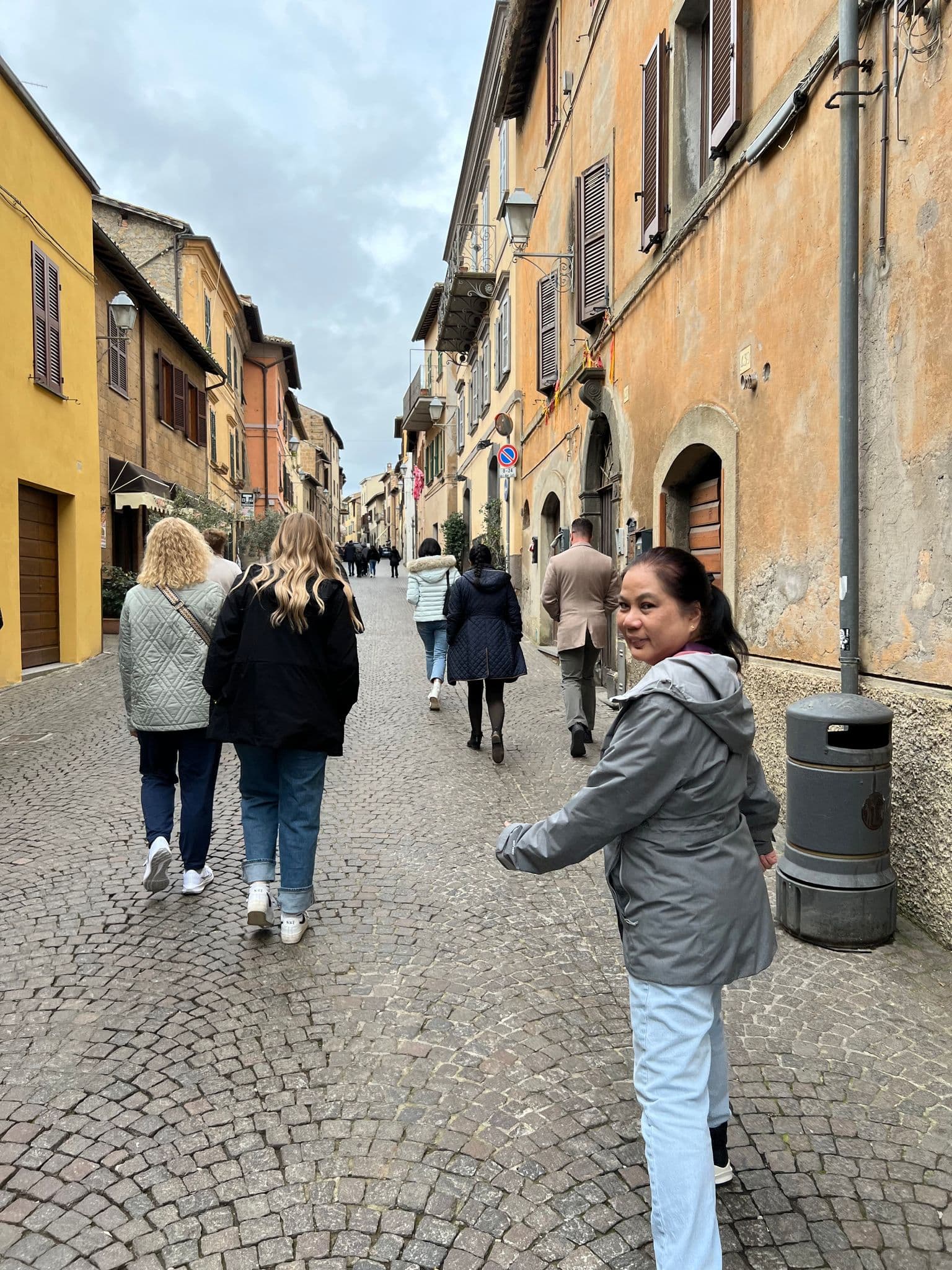 Cobblestone street in Orvieto, Umbria, Italy, with people walking and a woman glancing back.