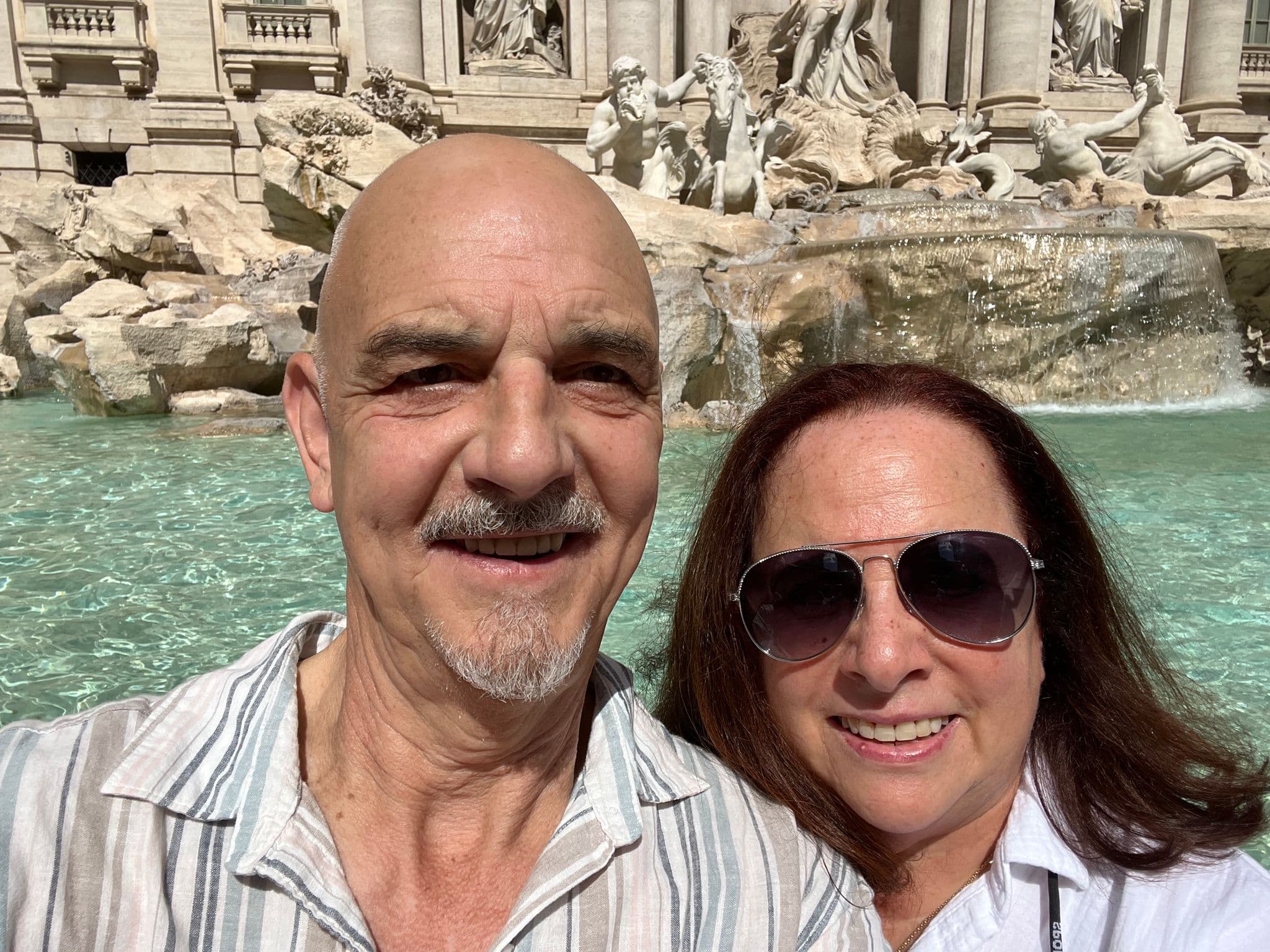 Trevi Fountain with two travelers taking a close selfie in front of the pool and baroque statues, Rome, Italy.