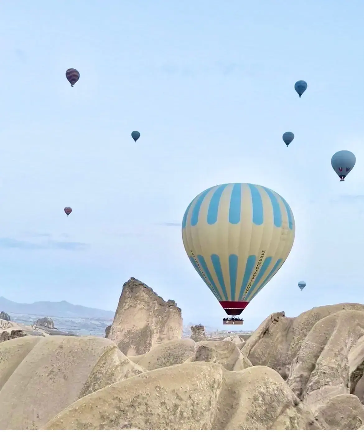 Striped hot air balloon floating above Cappadocia's rock formations and fairy chimneys, with other balloons in the sky, Turkey.