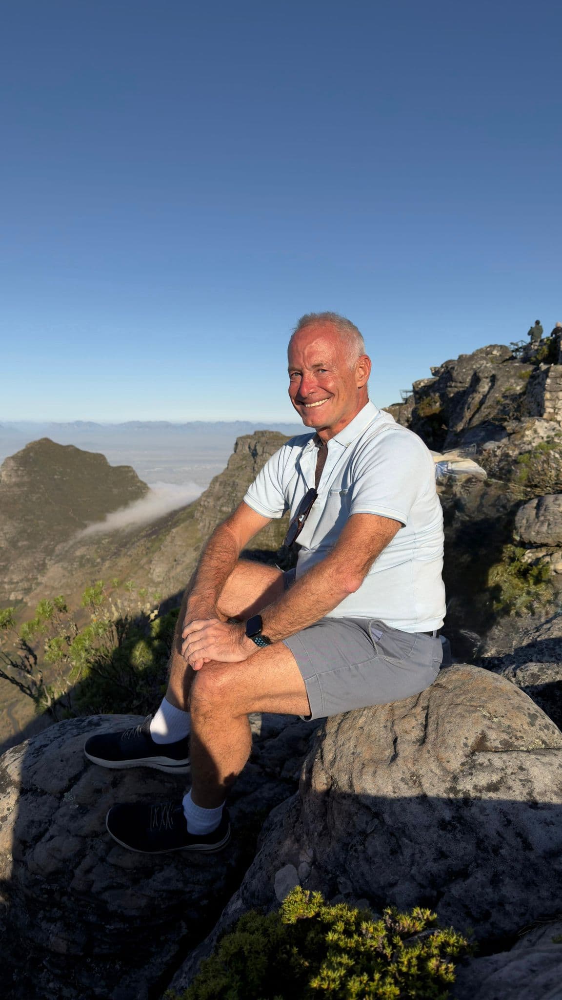 Table Mountain summit with a man sitting on a rock overlooking mountains and the ocean near Cape Town, South Africa.