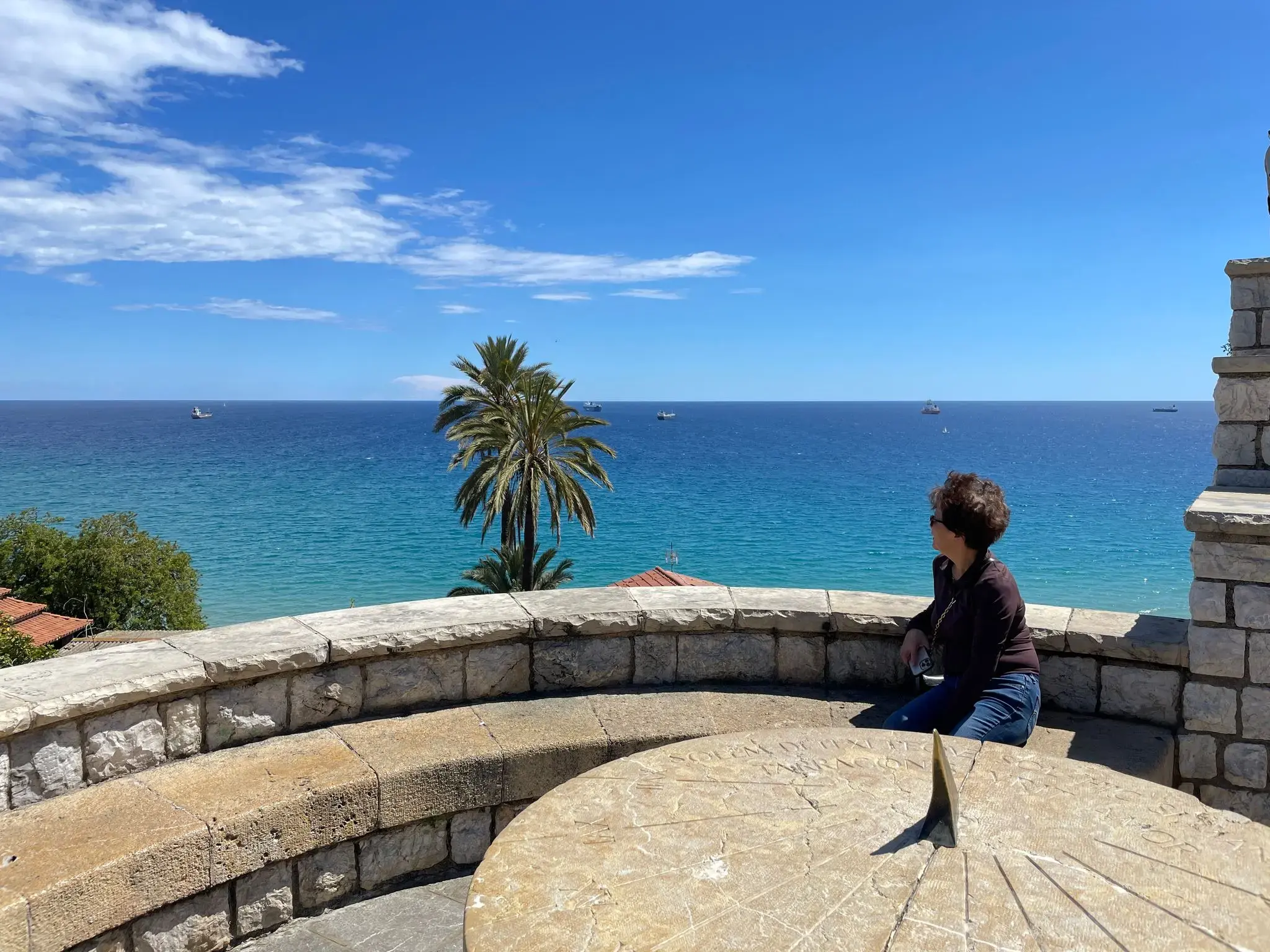 Balcony of the Mediterranean viewpoint in Tarragona, Spain, showing a person seated on a stone bench looking out toward the sea and a palm tree.
