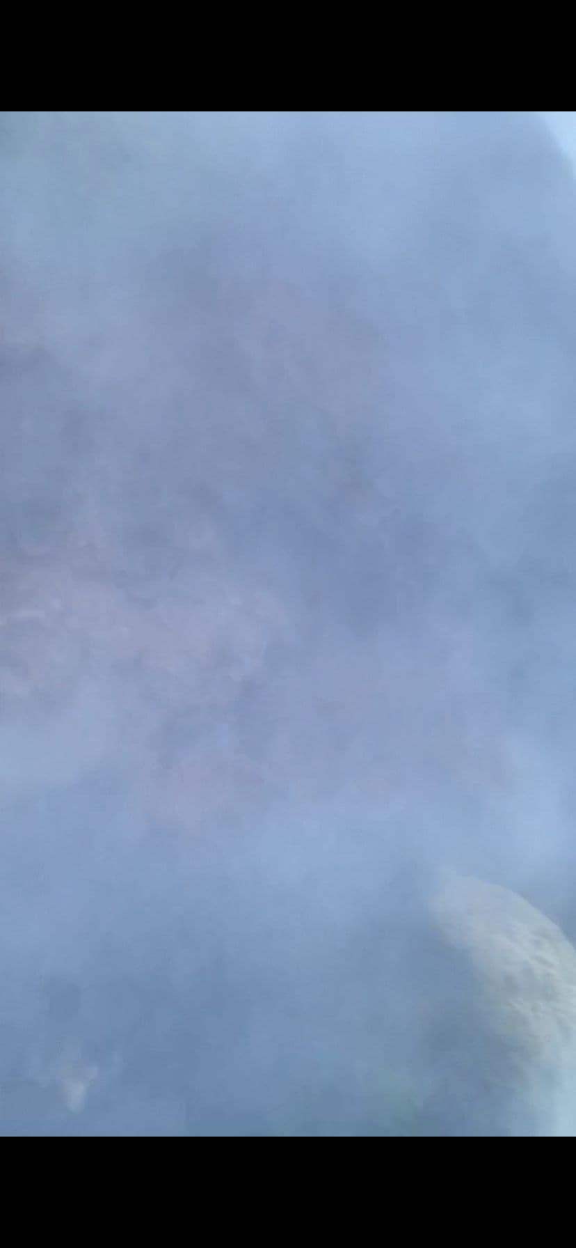 Thick steam and mist filling the frame with a pale rock at lower right, suggesting boiling water or hot vapor.