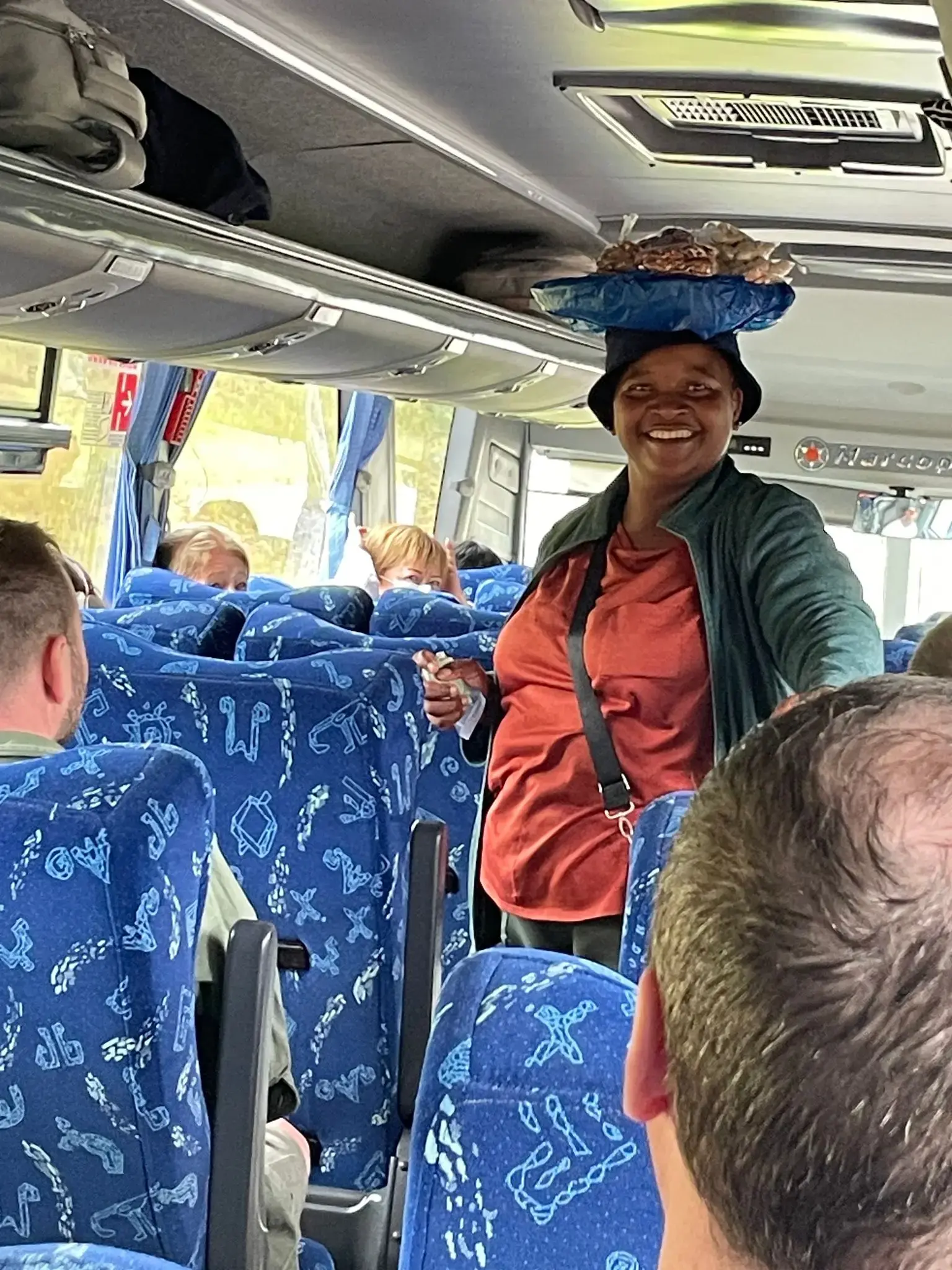 Woman selling macadamia nuts balancing a tray on her head inside a tour bus from Kruger National Park, South Africa.