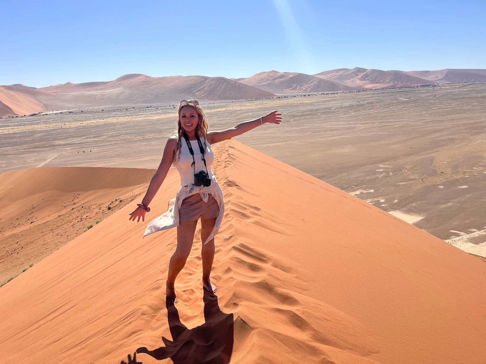 Dune 45 ridge with a traveler standing and gesturing on the sand in Sossusvlei, Namib Desert, Namibia.