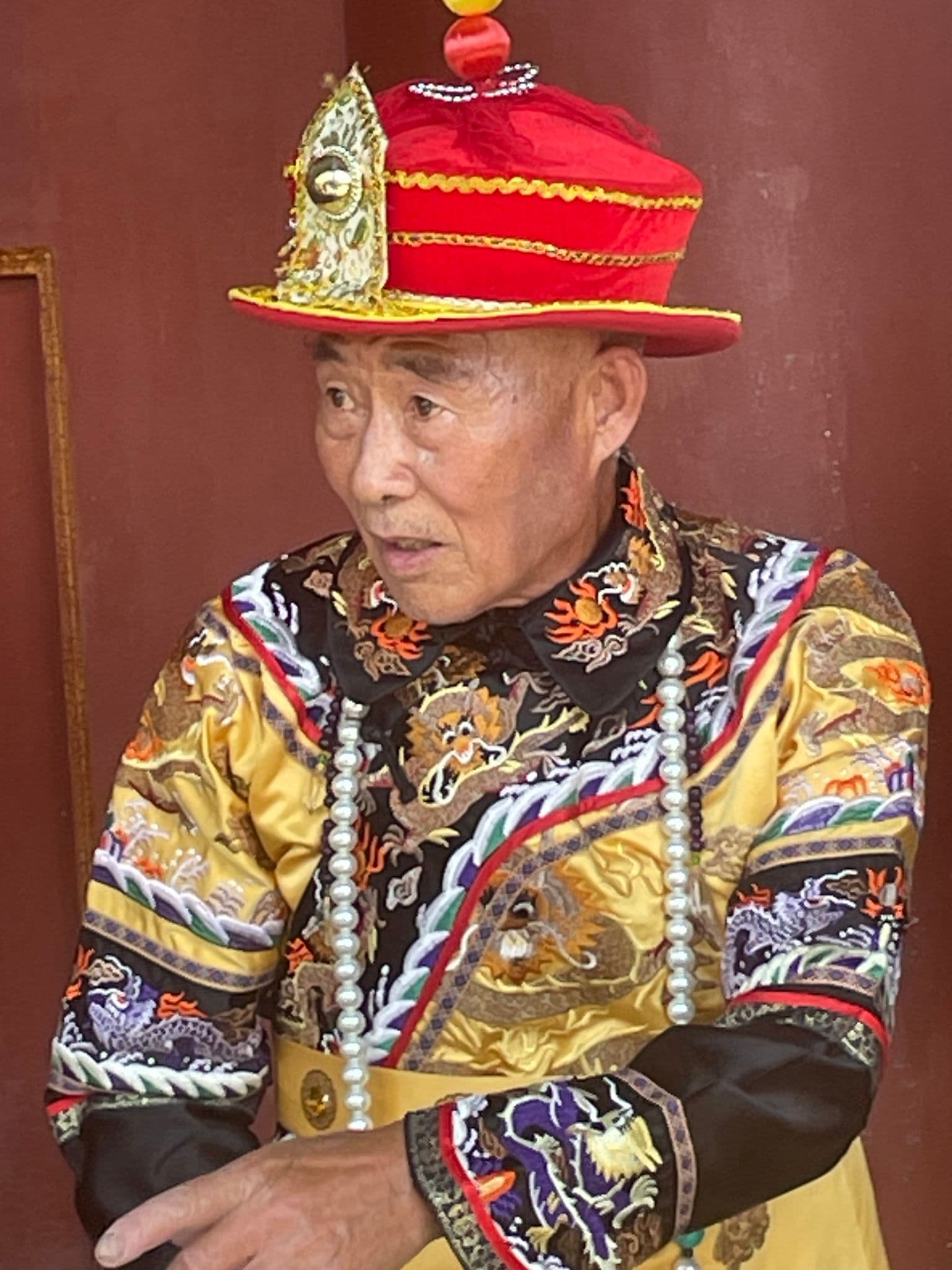 Man in ornate traditional Chinese costume standing by a red temple wall at the Temple of Heaven, Beijing, China.