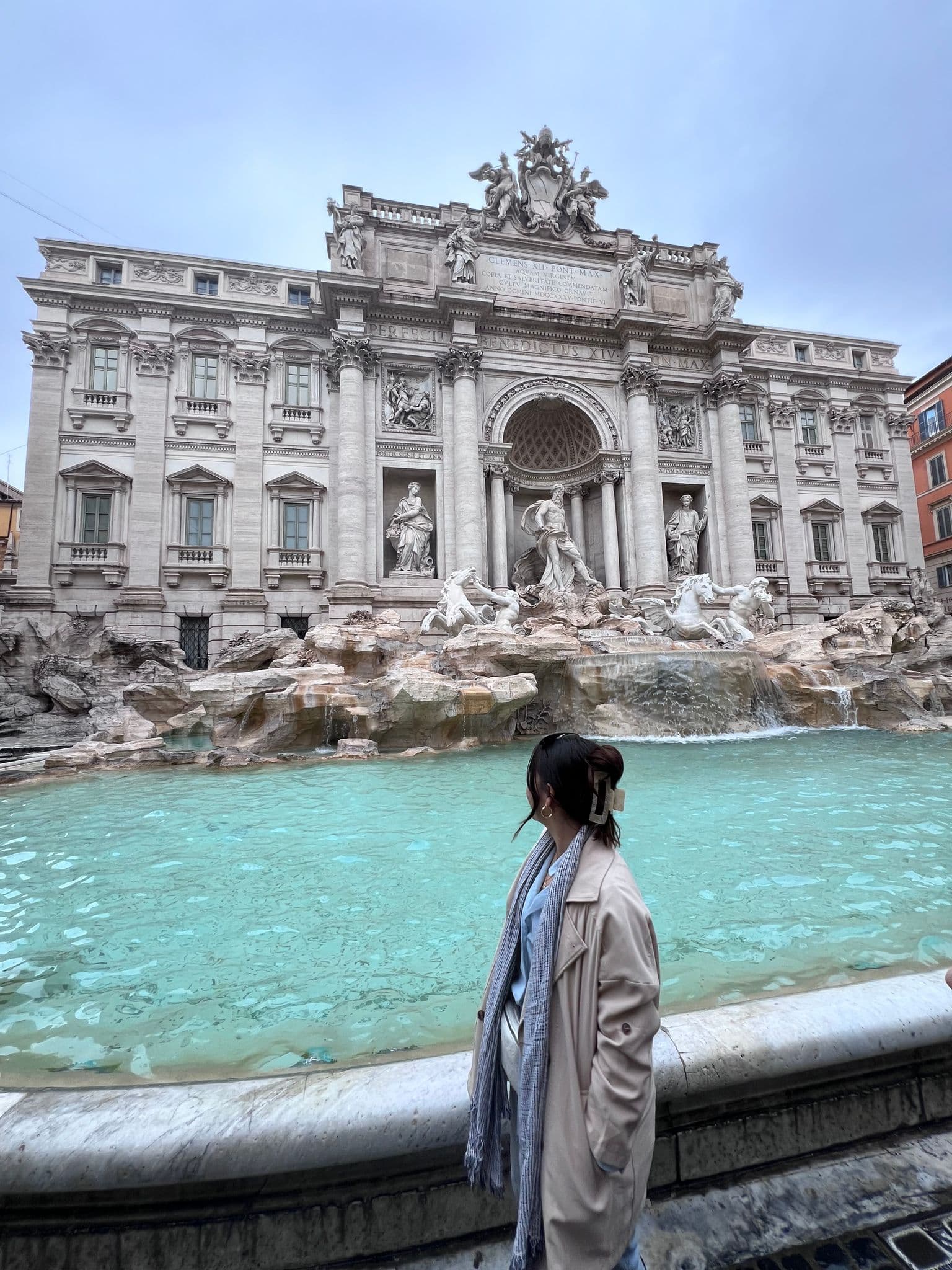 Trevi Fountain in Rome with a person standing at the pool edge looking toward the sculptures and turquoise water.