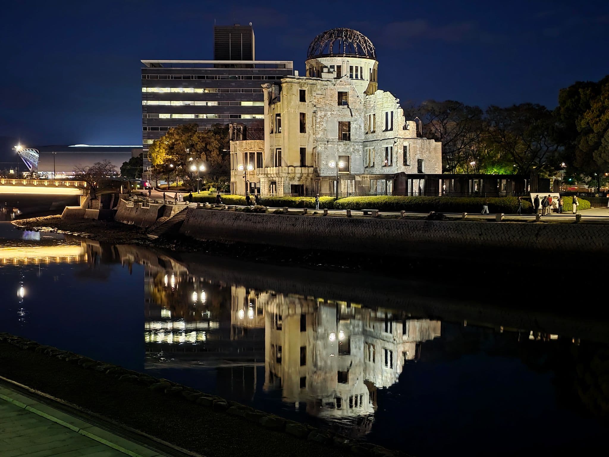 Hiroshima Peace Memorial (Genbaku Dome) reflected in the river at night with people walking along the riverside in Hiroshima, Japan.
