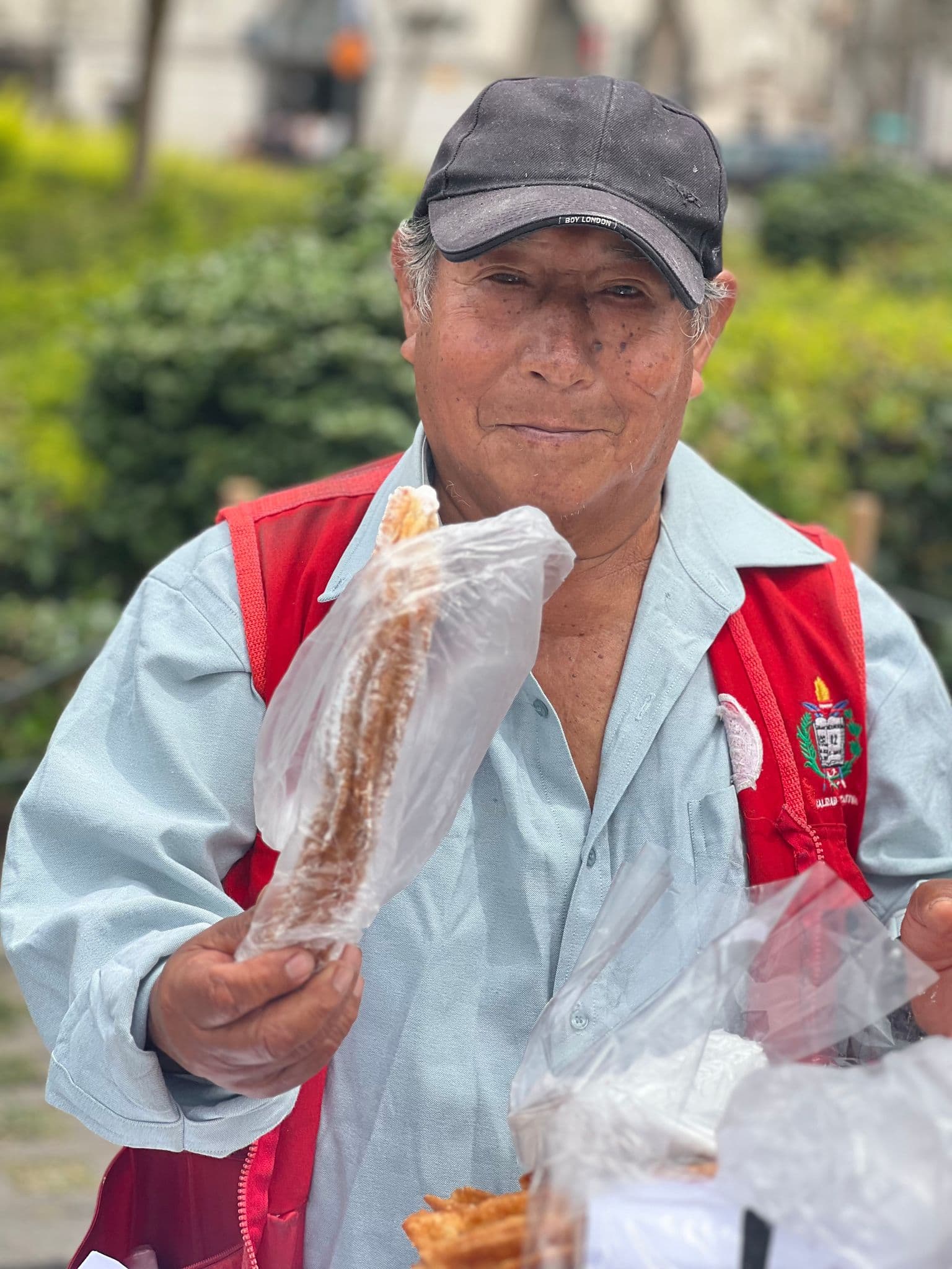 Street vendor holding a wrapped pastry in Plaza San Martín, Lima, Peru, offering it to the camera.