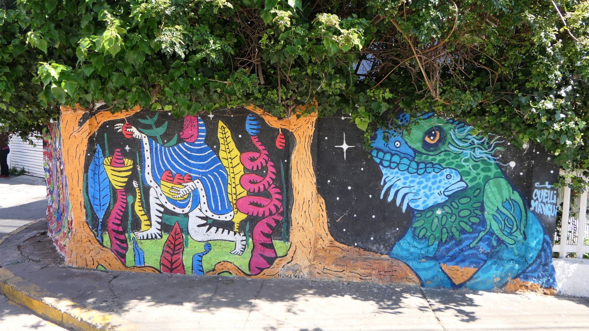 Colorful street mural of abstract creatures framed by overhanging ivy on a Valparaíso street, Chile.