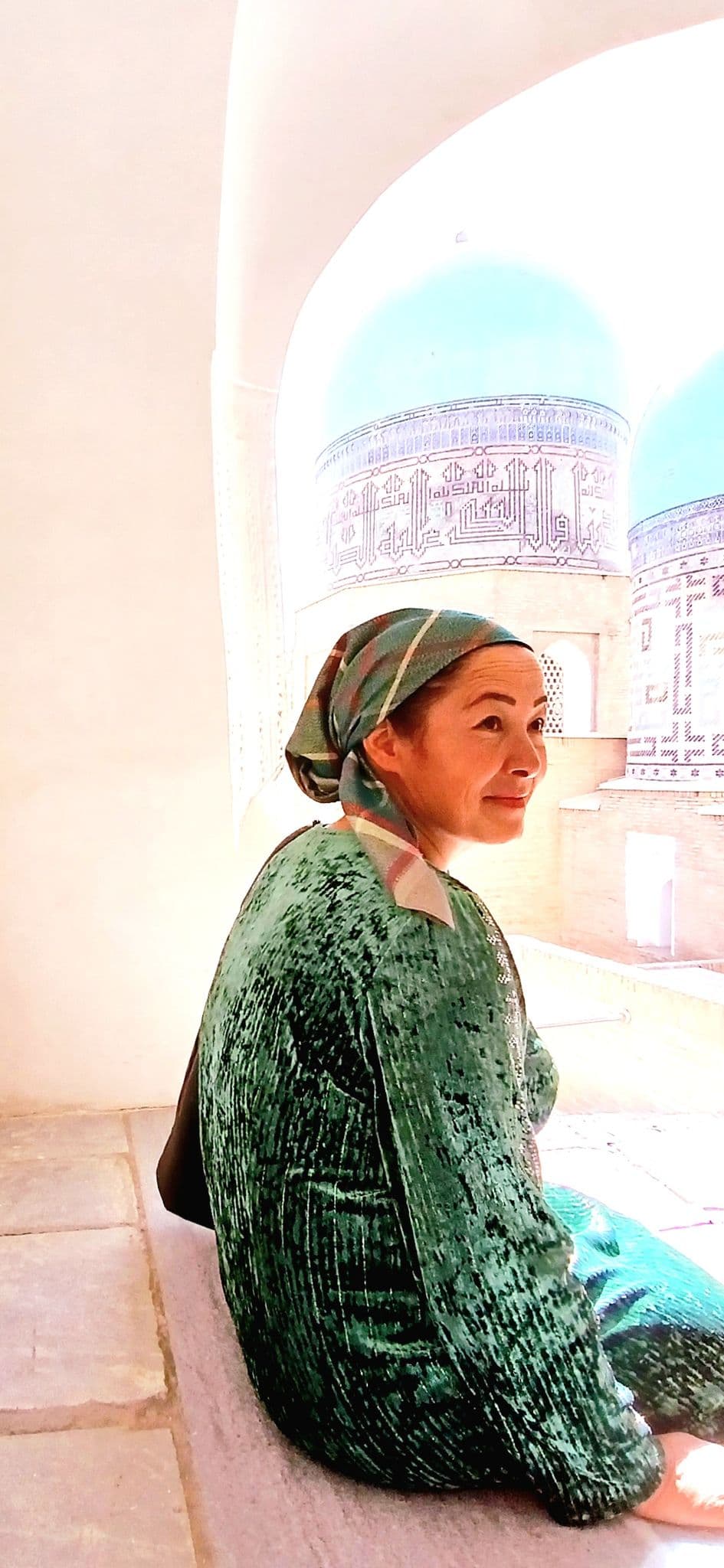 Shah-i-Zinda mausoleums in Samarkand, Uzbekistan, with a woman in a headscarf sitting in an arched niche.