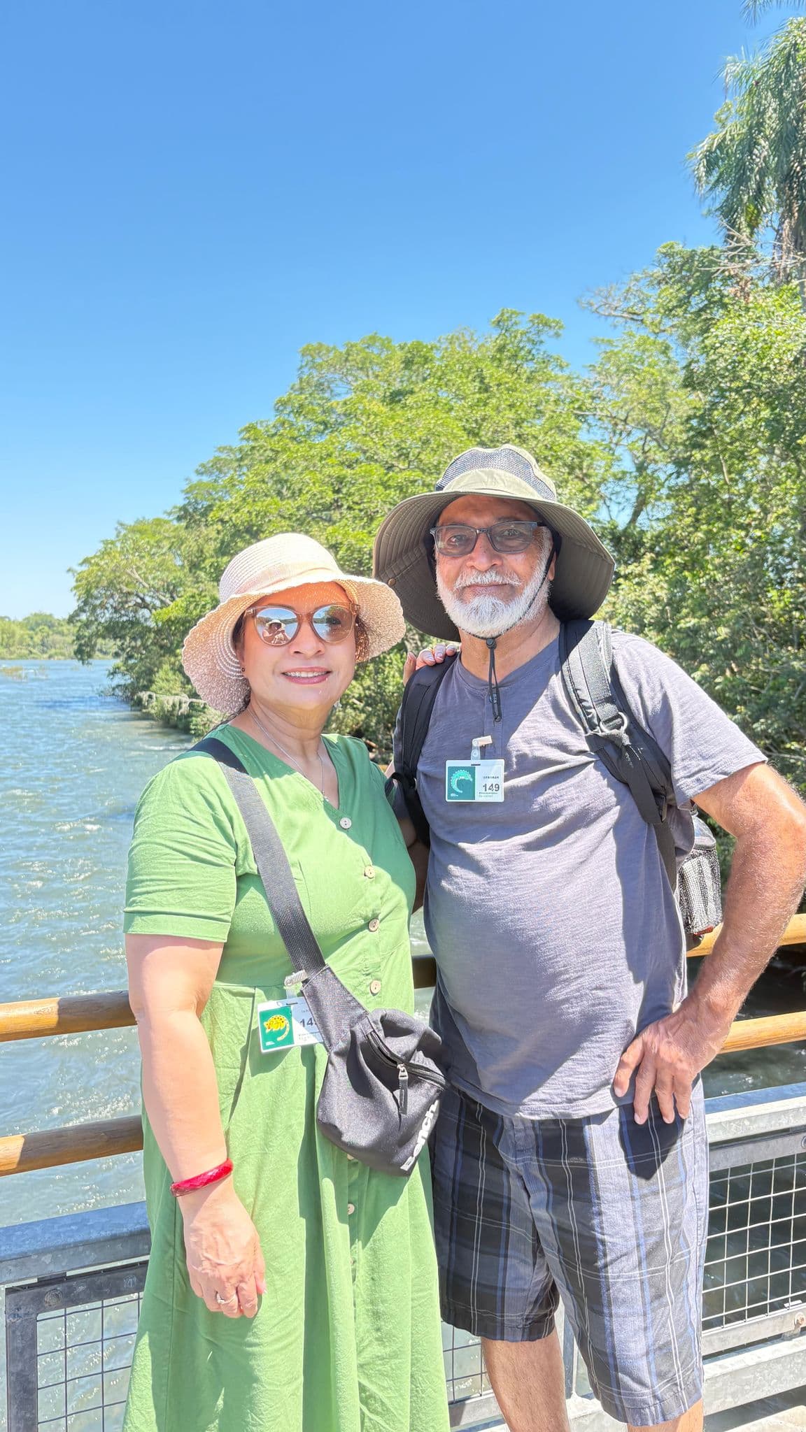 A couple posing on a riverside viewing platform with water and trees behind them near Iguazu Falls