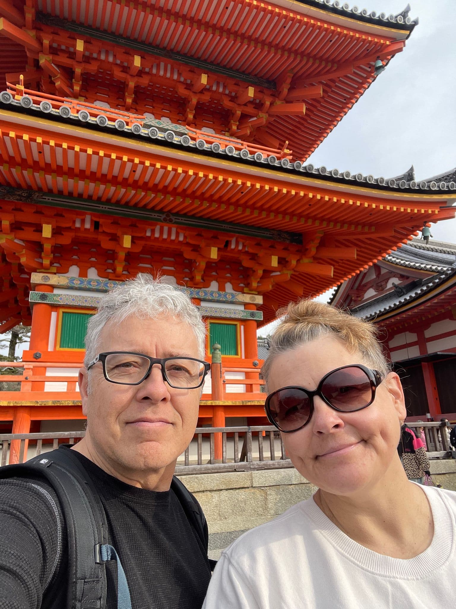 Kiyomizu-dera Temple's bright vermilion building with two travelers taking a selfie in Kyoto, Japan.