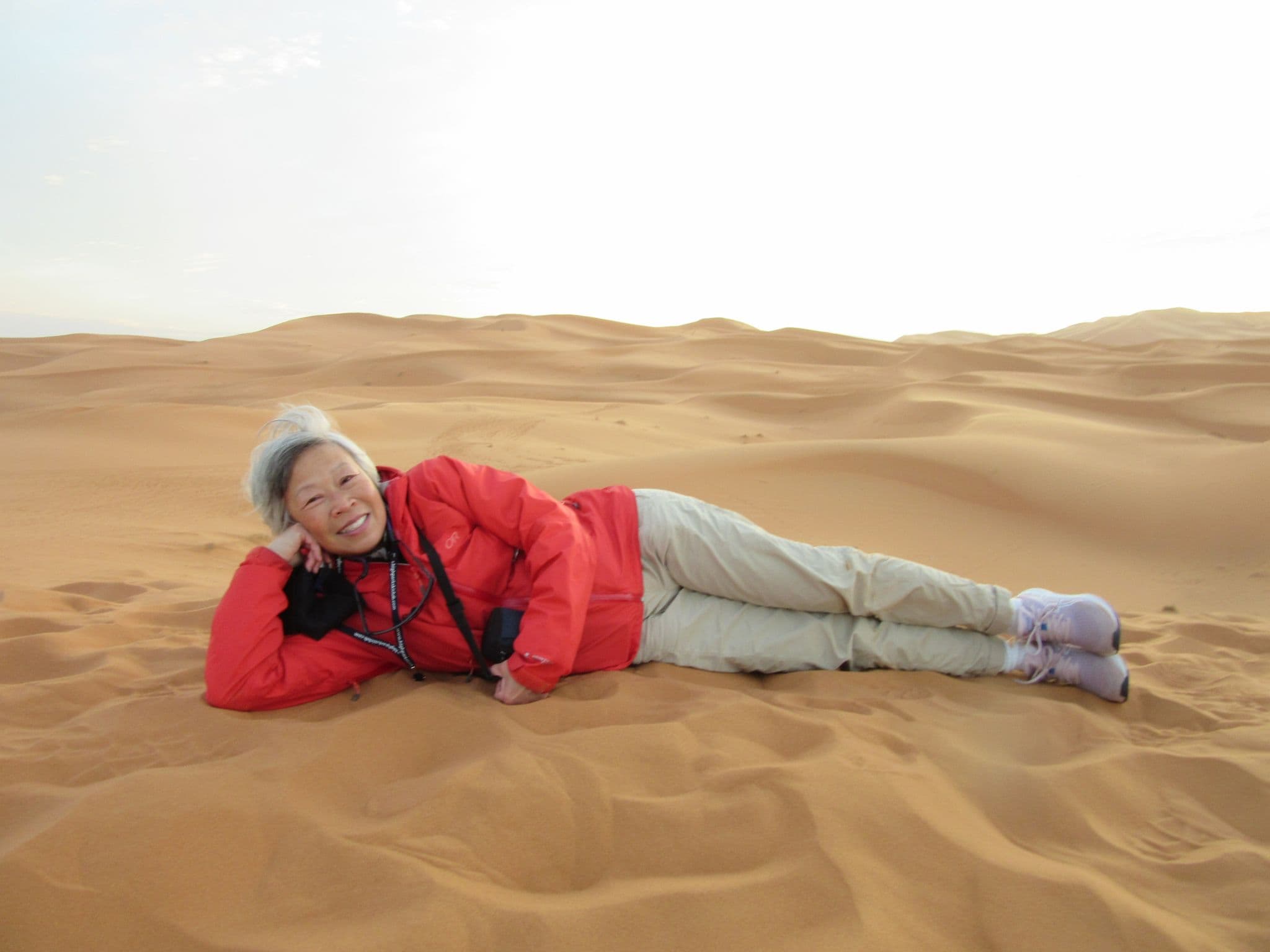Sahara Desert sand dunes with a traveler reclining on the sand wearing a red jacket, Morocco.