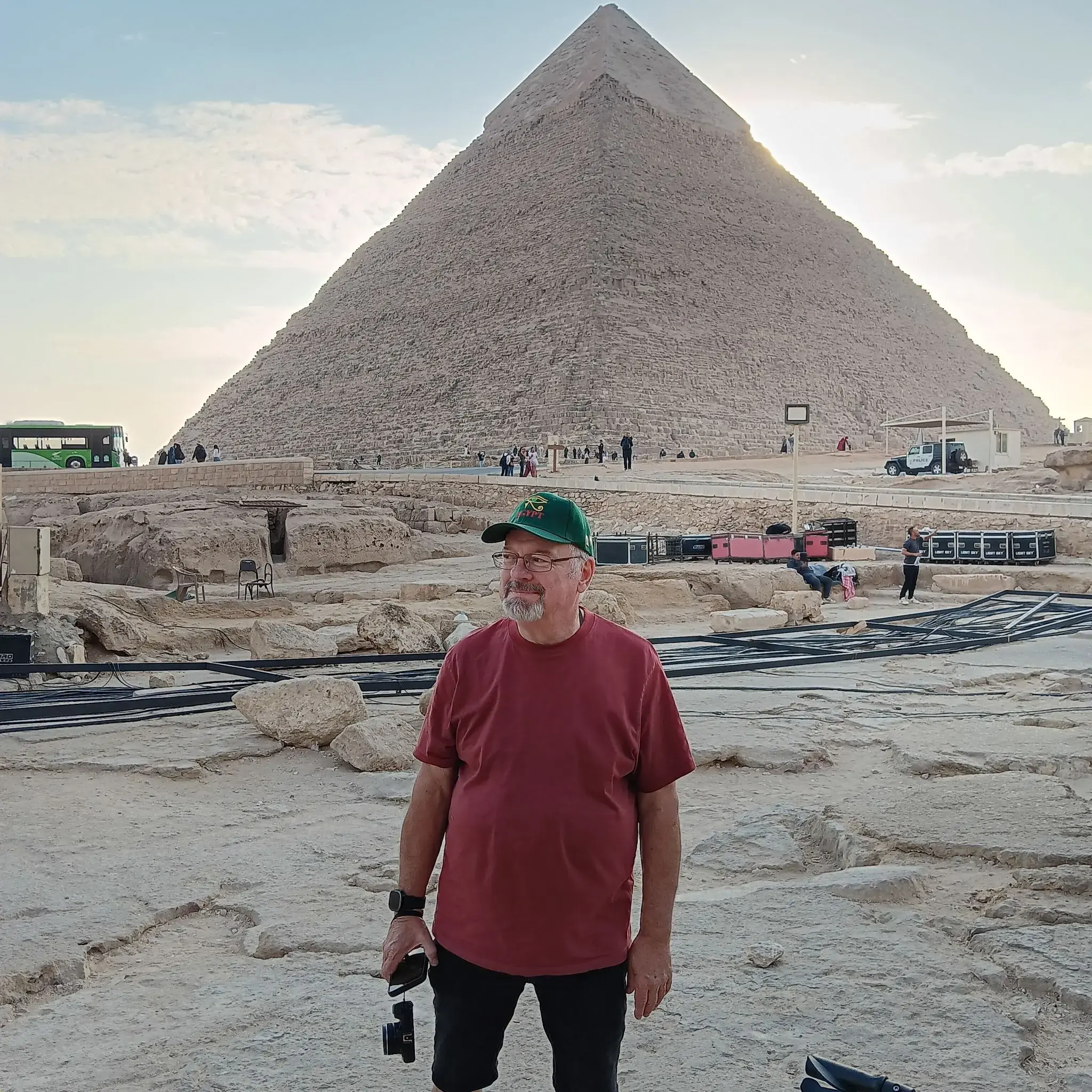 Great Pyramid of Giza towering behind a man standing and holding a camera on a trip in Giza, Egypt.