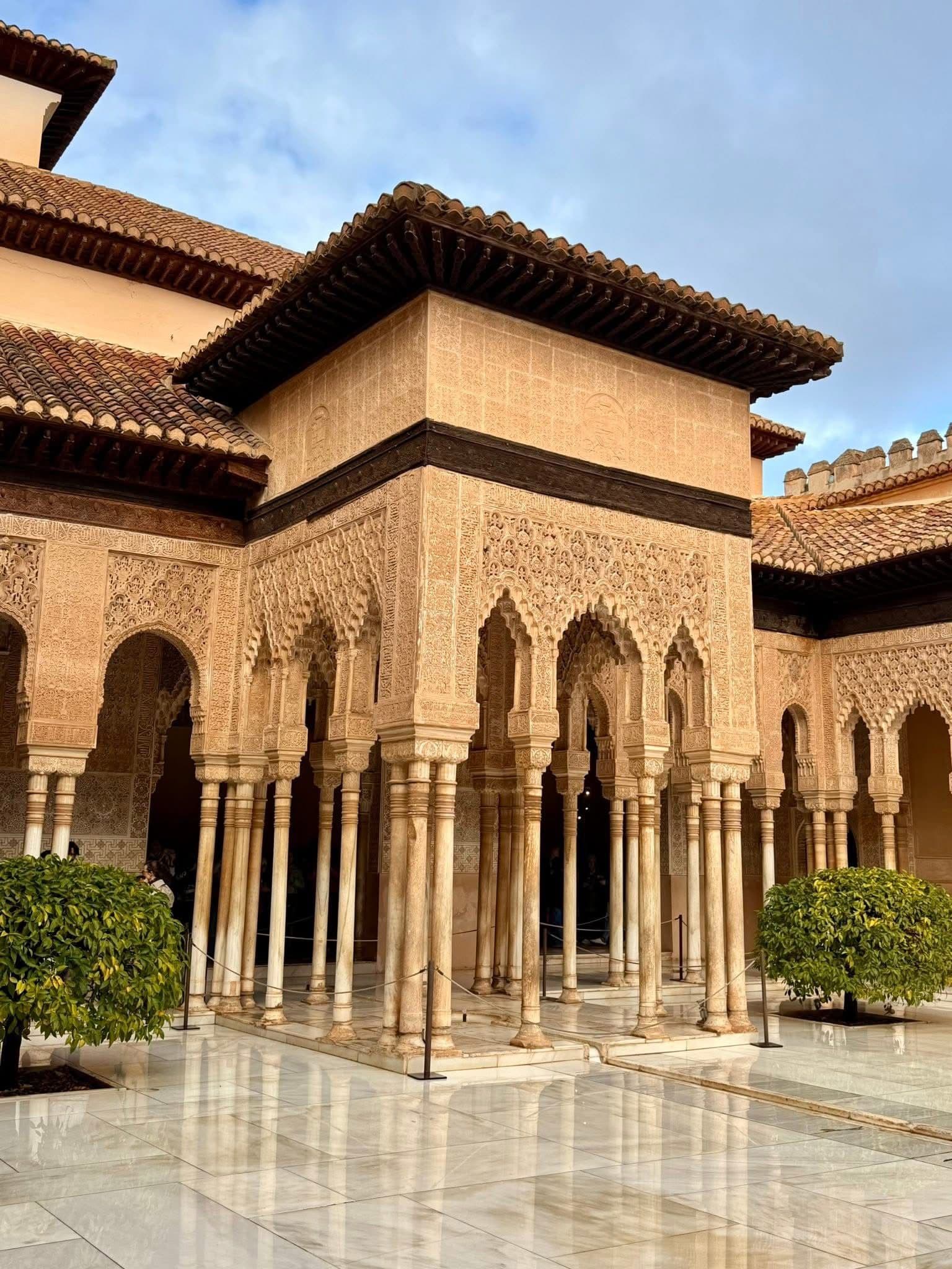 Court of the Lions at the Alhambra in Granada, Spain, showing carved Moorish arches and slender columns around a polished marble courtyard.
